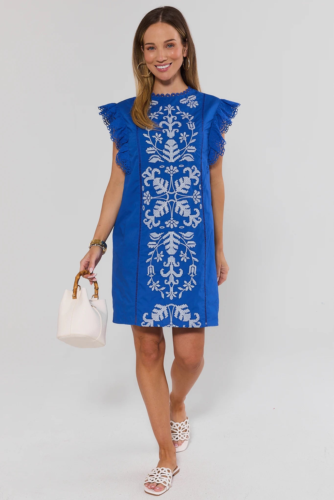 Woman wearing a blue dress with white floral patterns on a gray background walking