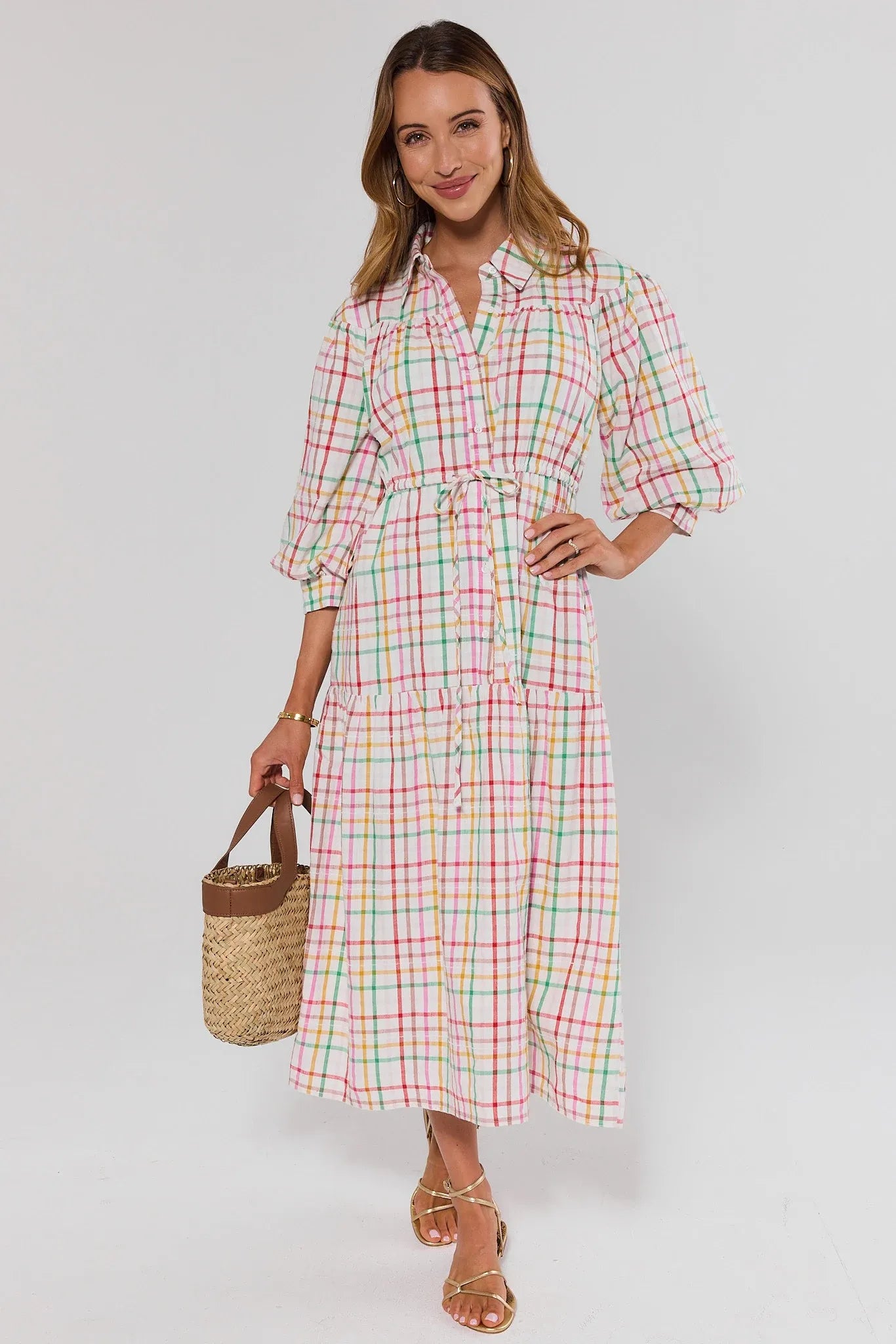 Woman wearing a plaid dress holding a straw bag on a white background