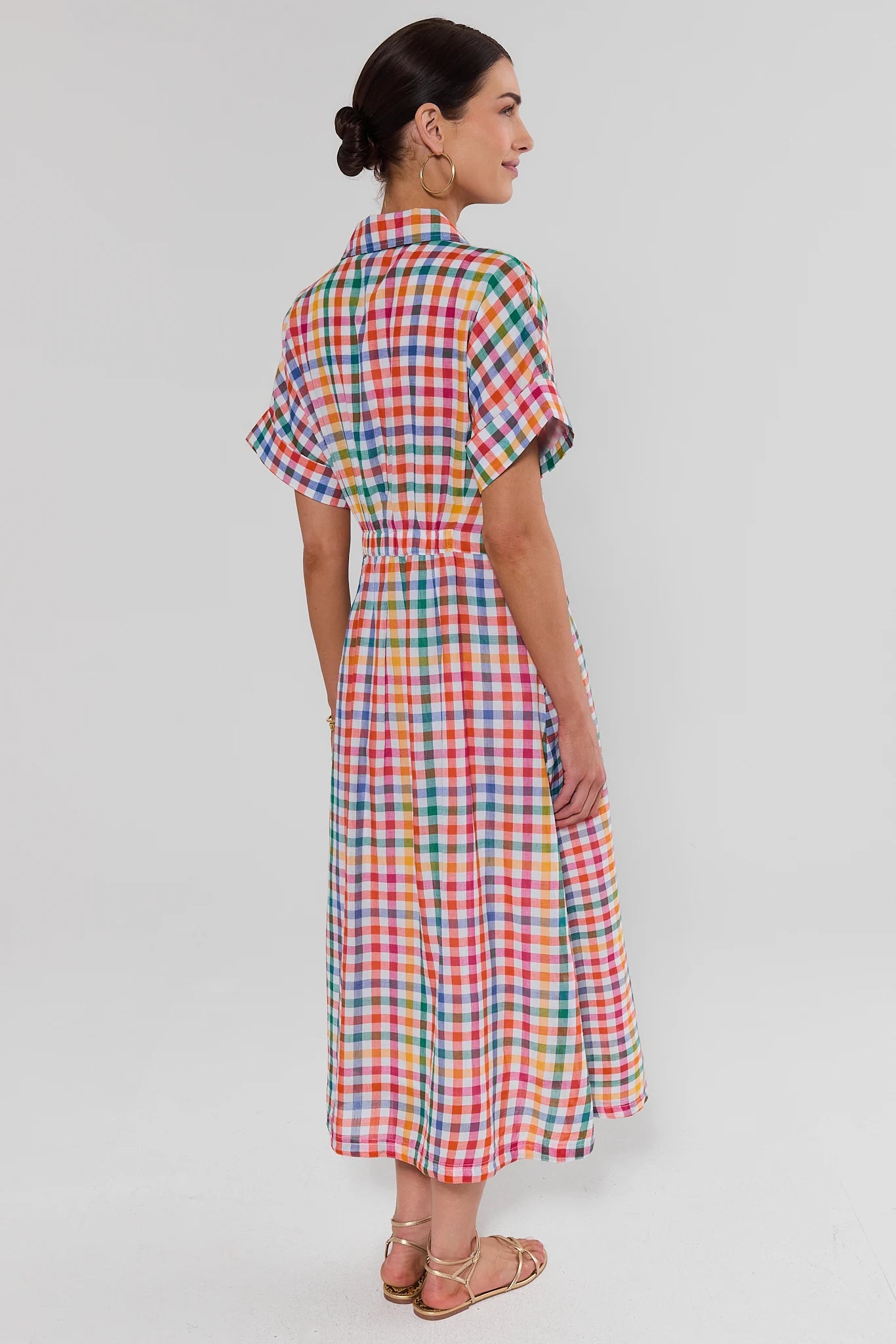 Woman standing wearing a colorful checkered dress on a light gray background