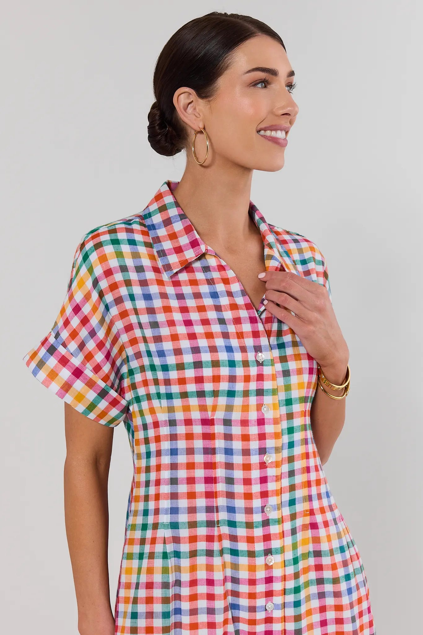 Woman wearing a colorful checkered shirt dress against a plain background close up