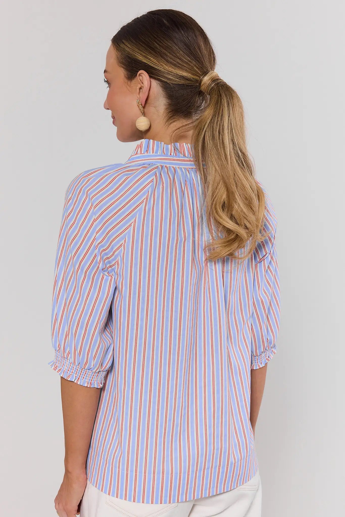 Woman wearing a striped shirt against a plain background standing