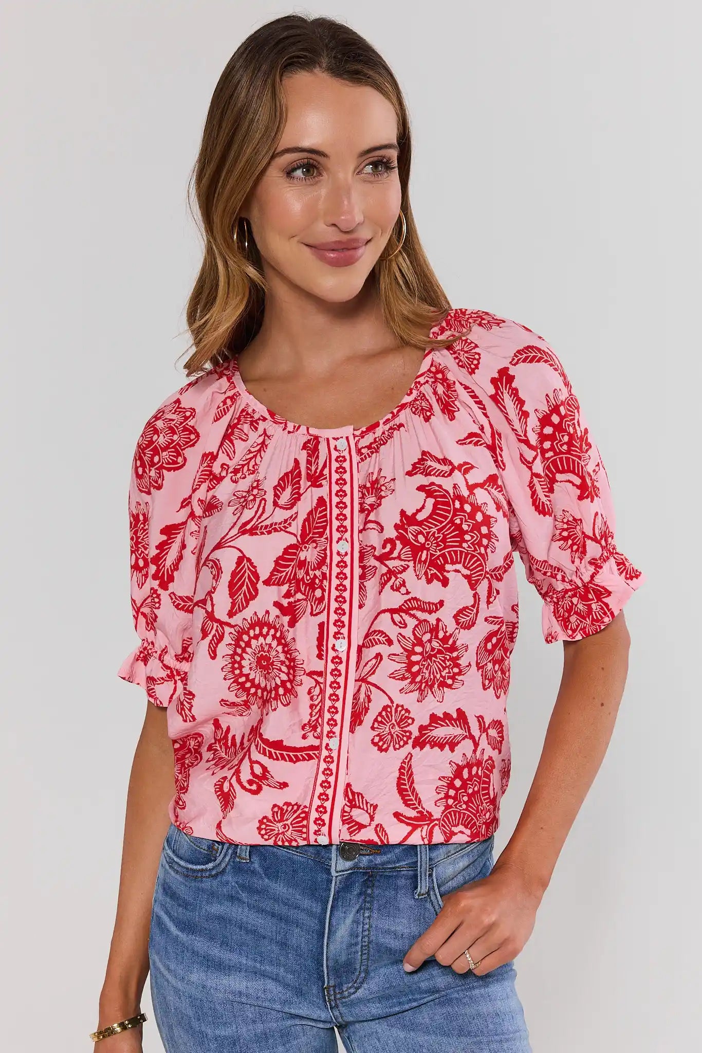 Woman wearing a pink floral blouse with red patterns on a white background