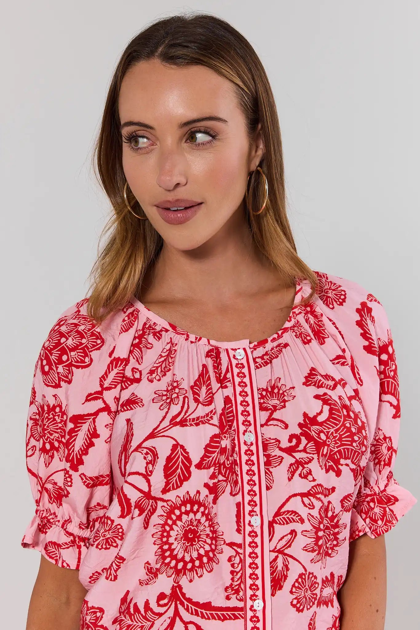 close up Woman wearing a pink blouse with red floral patterns on a plain background