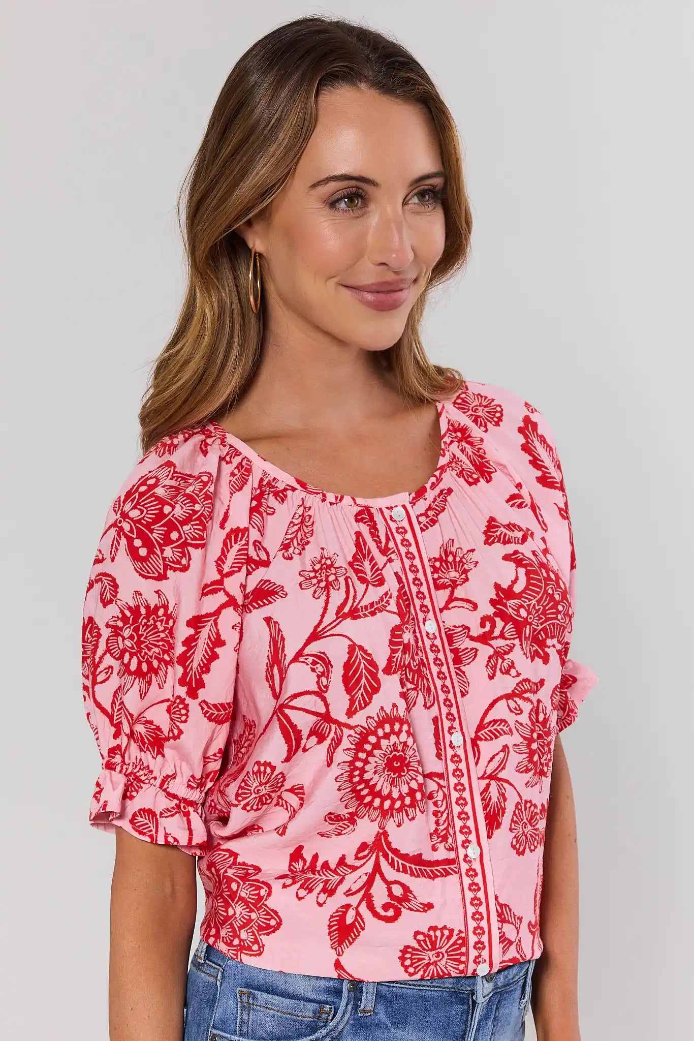 Woman wearing a pink floral blouse with red patterns on a plain background side