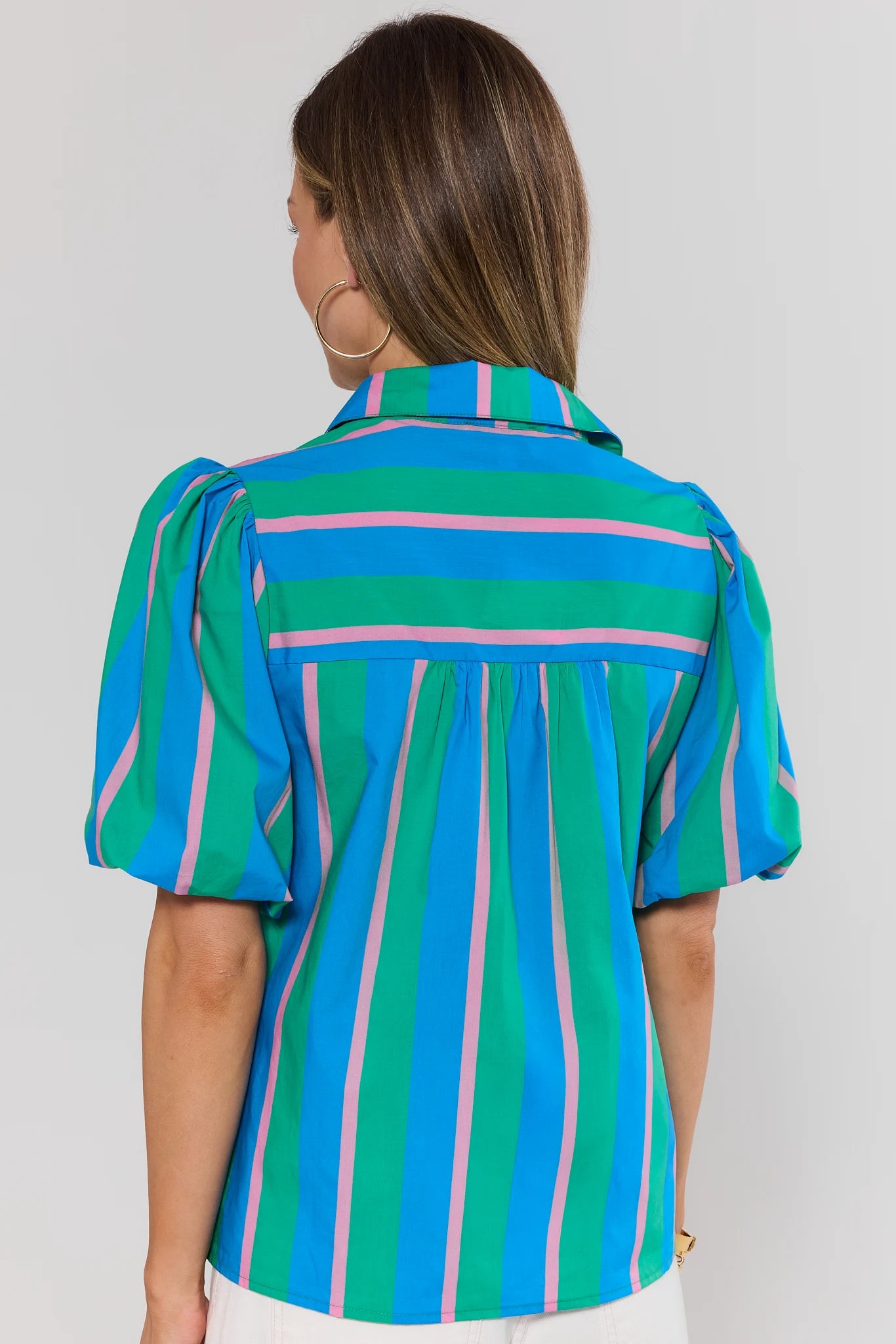Woman wearing a colorful striped shirt against a plain background stand