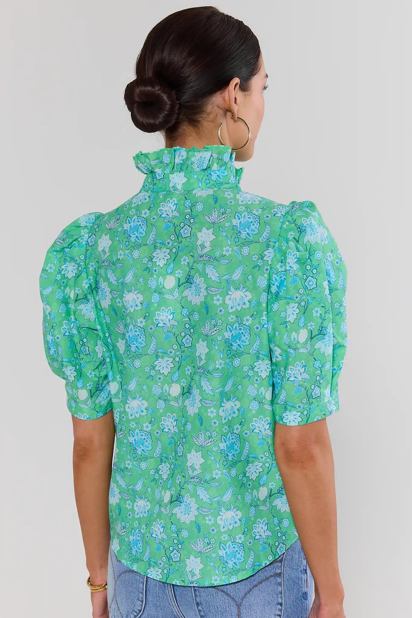 Person standing wearing a green floral blouse against a white background