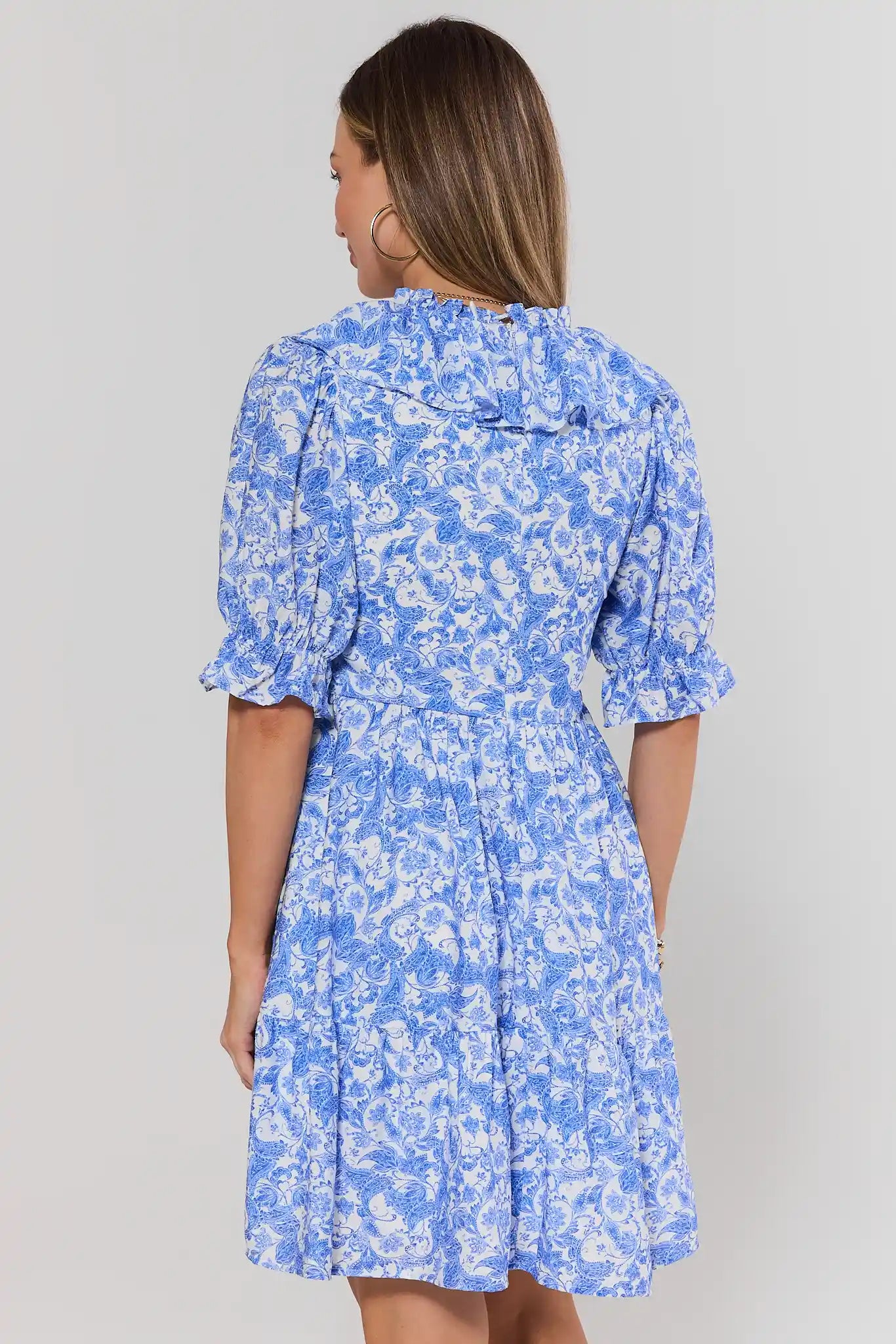Woman standing wearing a blue floral dress against a gray background