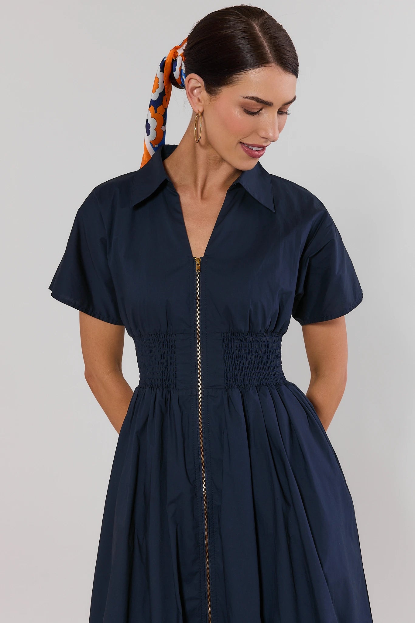 Woman wearing a navy dress with a plain background close up