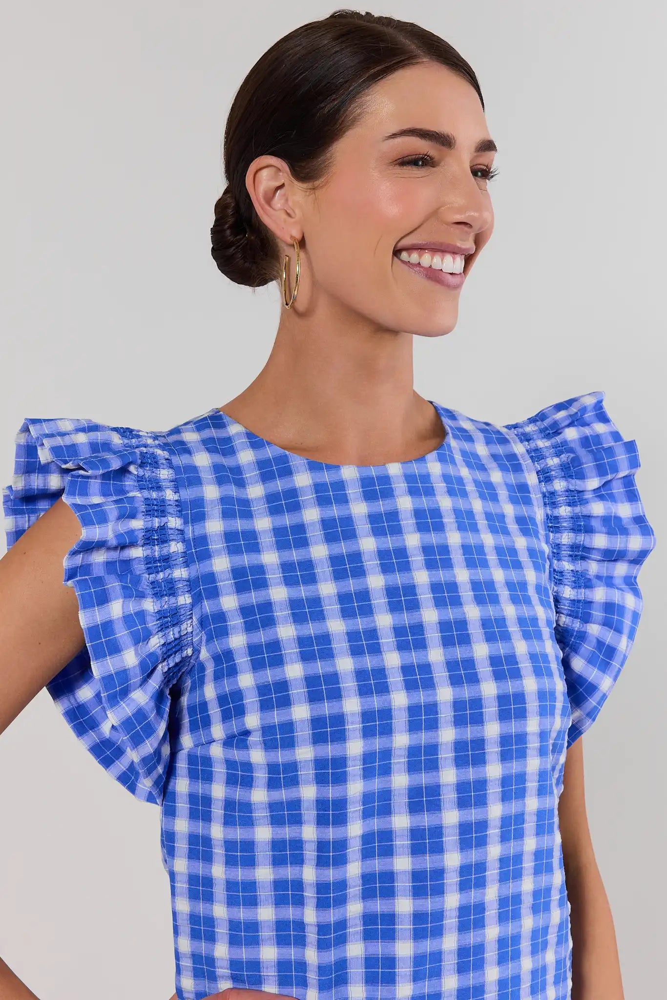 close up Woman wearing a blue and white checkered top against a plain background