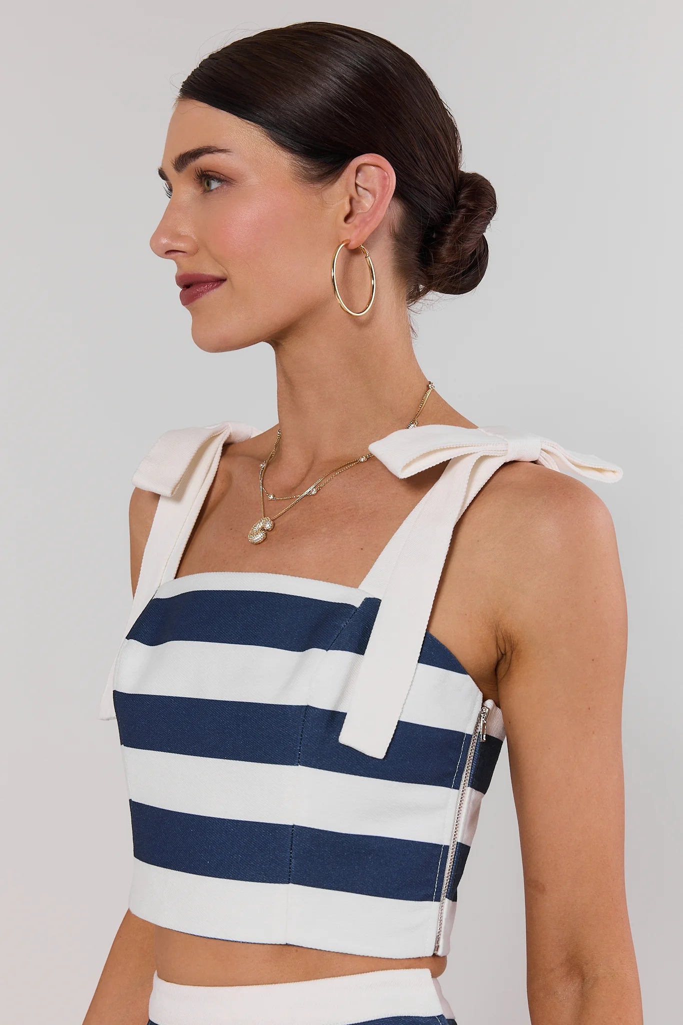 Woman wearing a blue and white striped top with bow straps against a plain background side