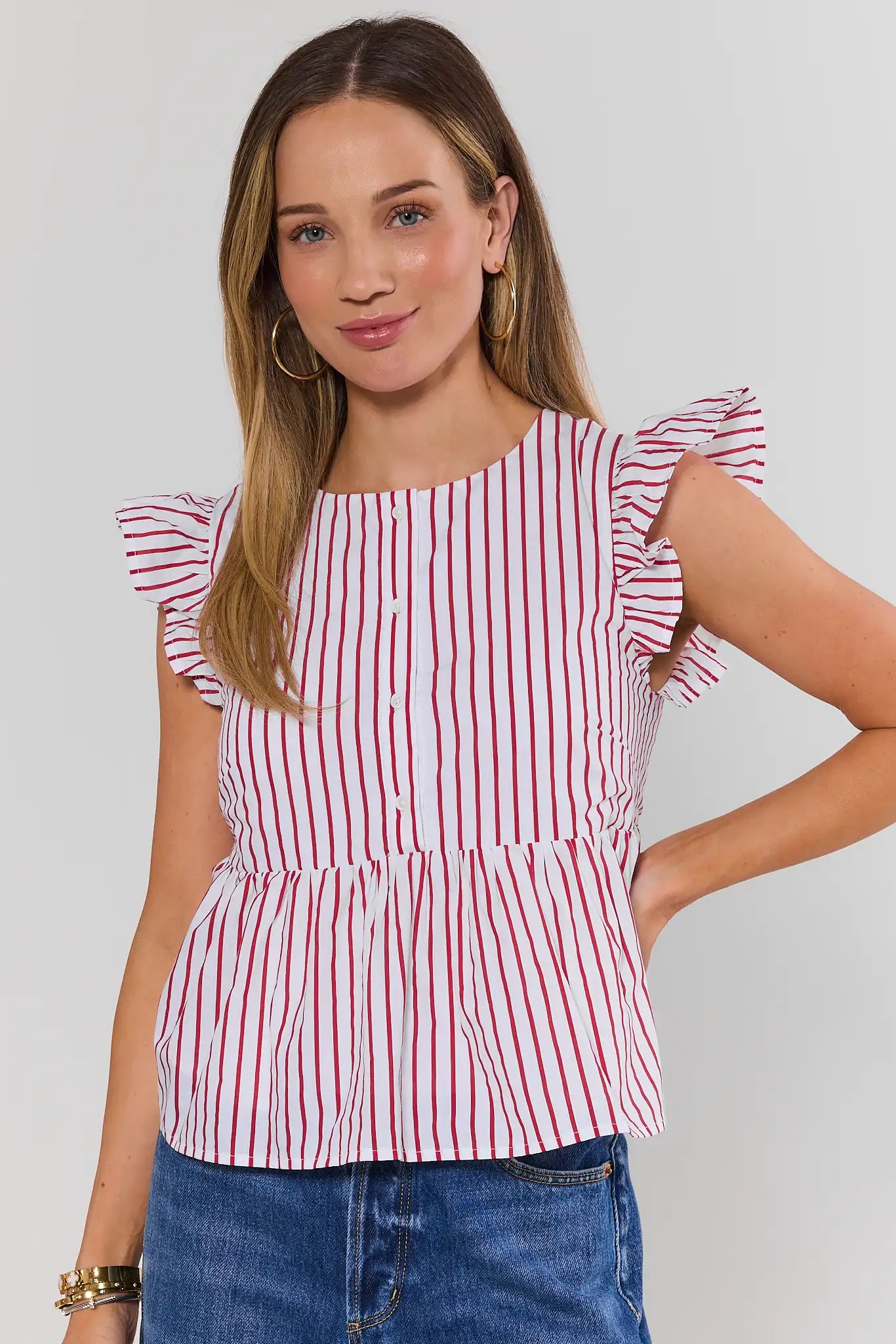 Woman wearing a red and white striped top with ruffled sleeves on a plain background