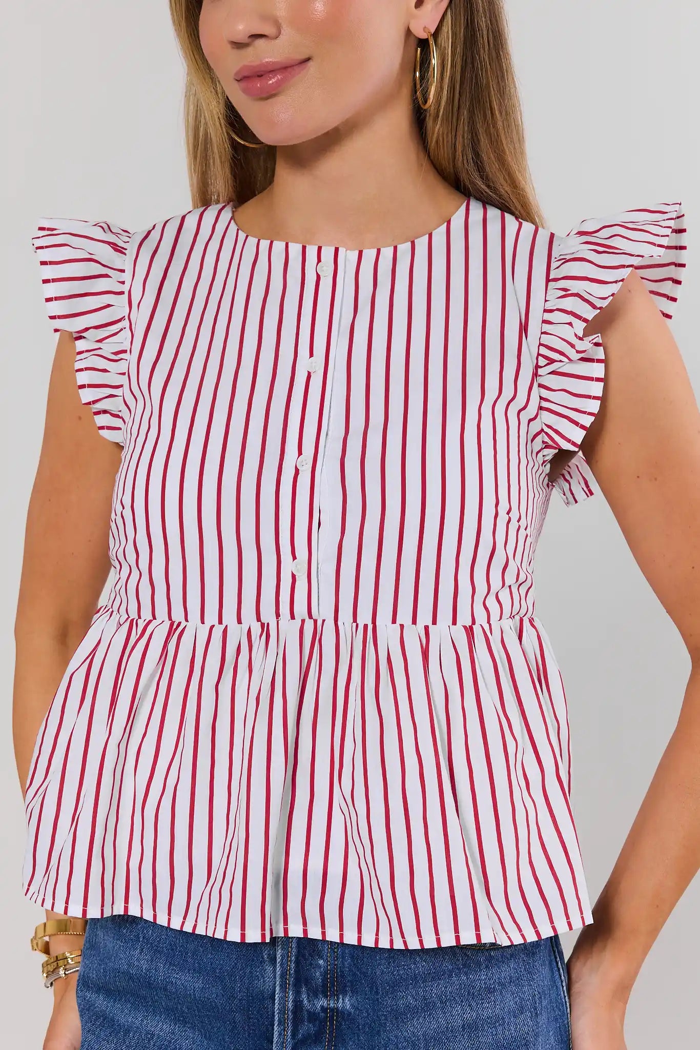 Woman wearing a red and white striped top with ruffled sleeves against a plain background close up