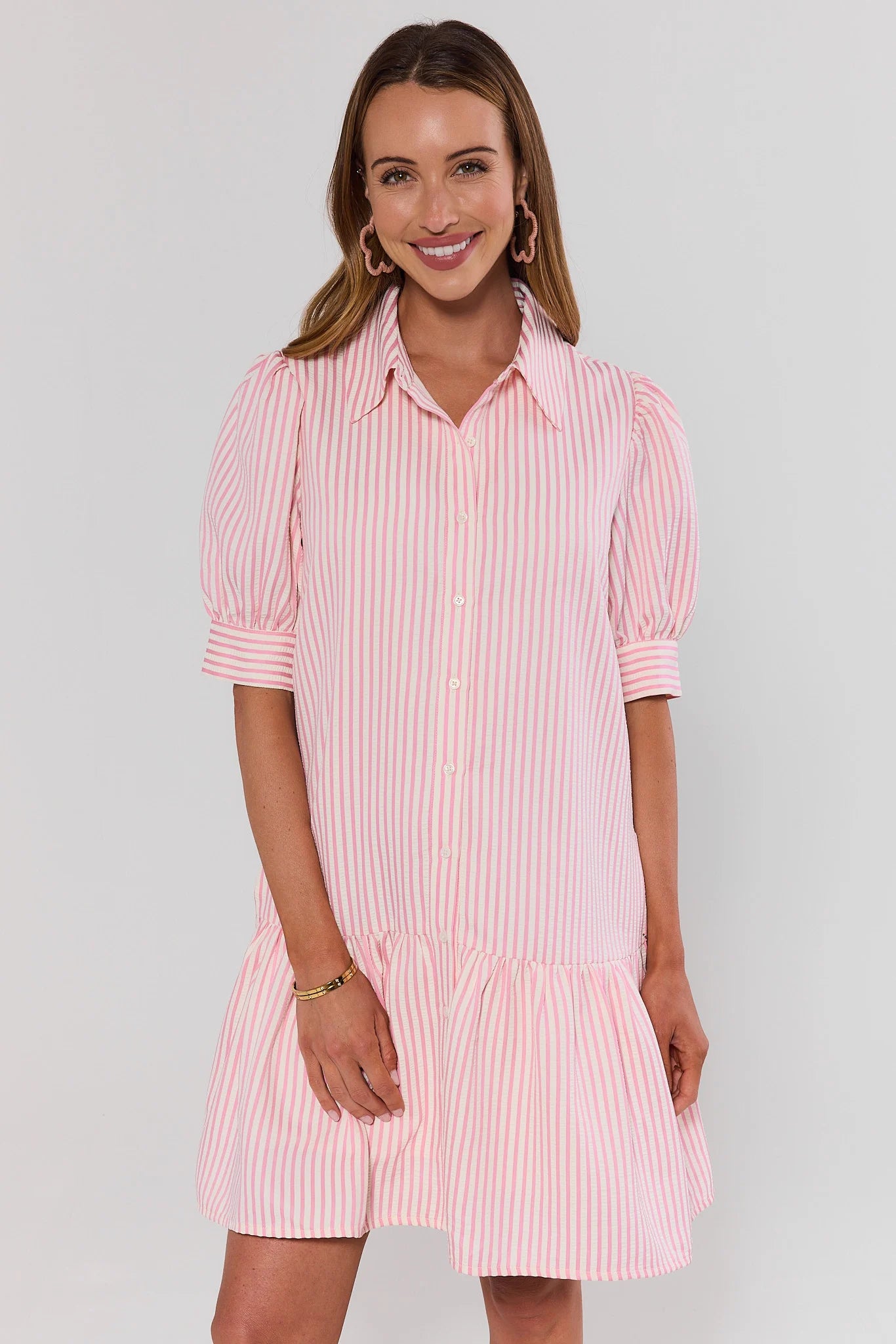 Woman wearing a pink and white striped dress against a gray background standing