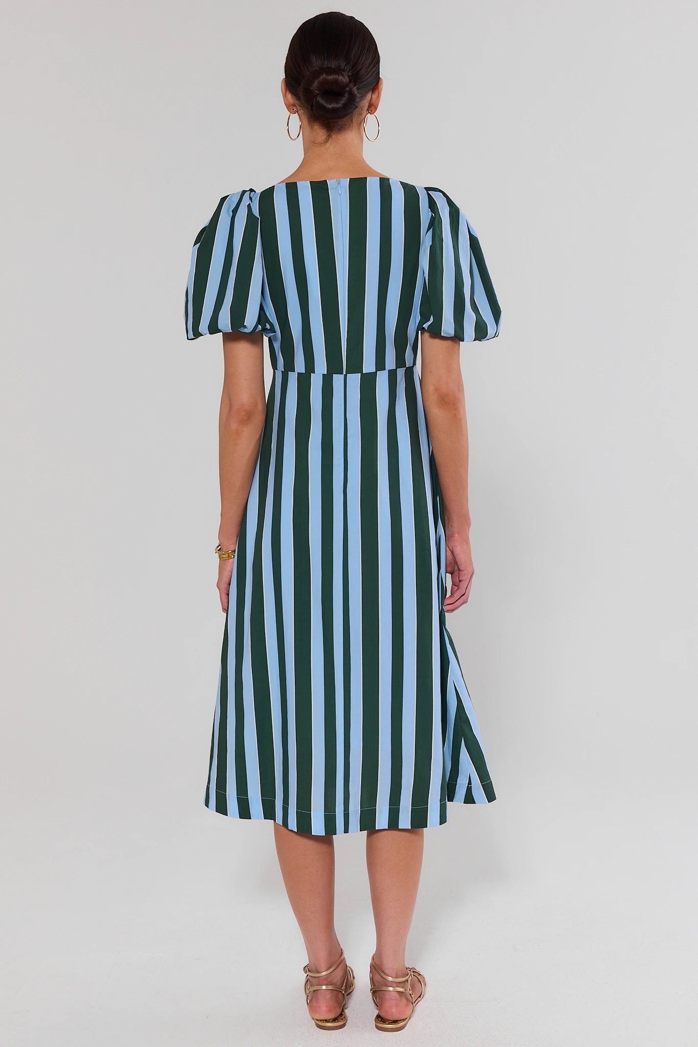 Woman standing wearing a green and blue striped dress on a white background