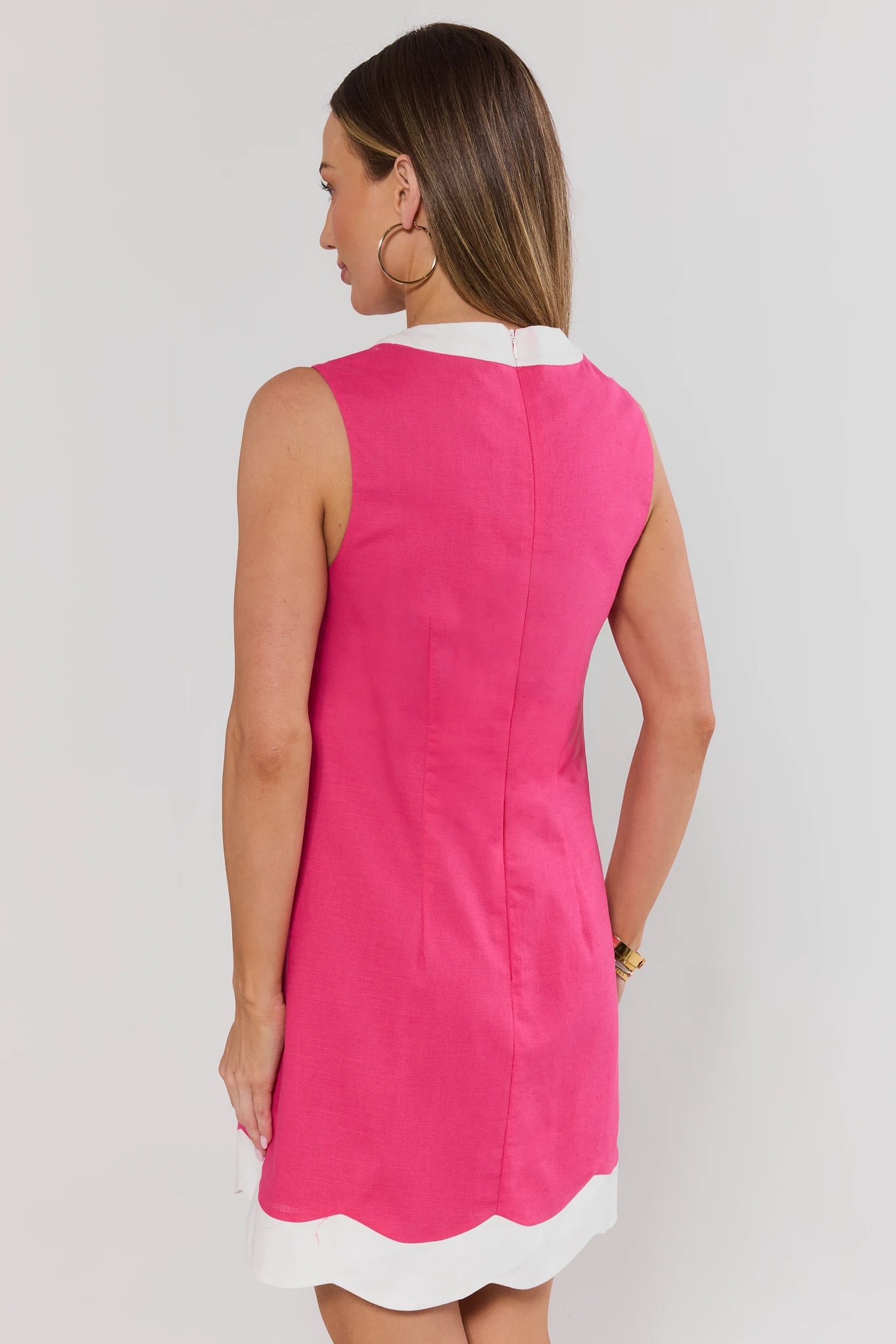 Woman wearing a pink dress with white trim on a plain background standing