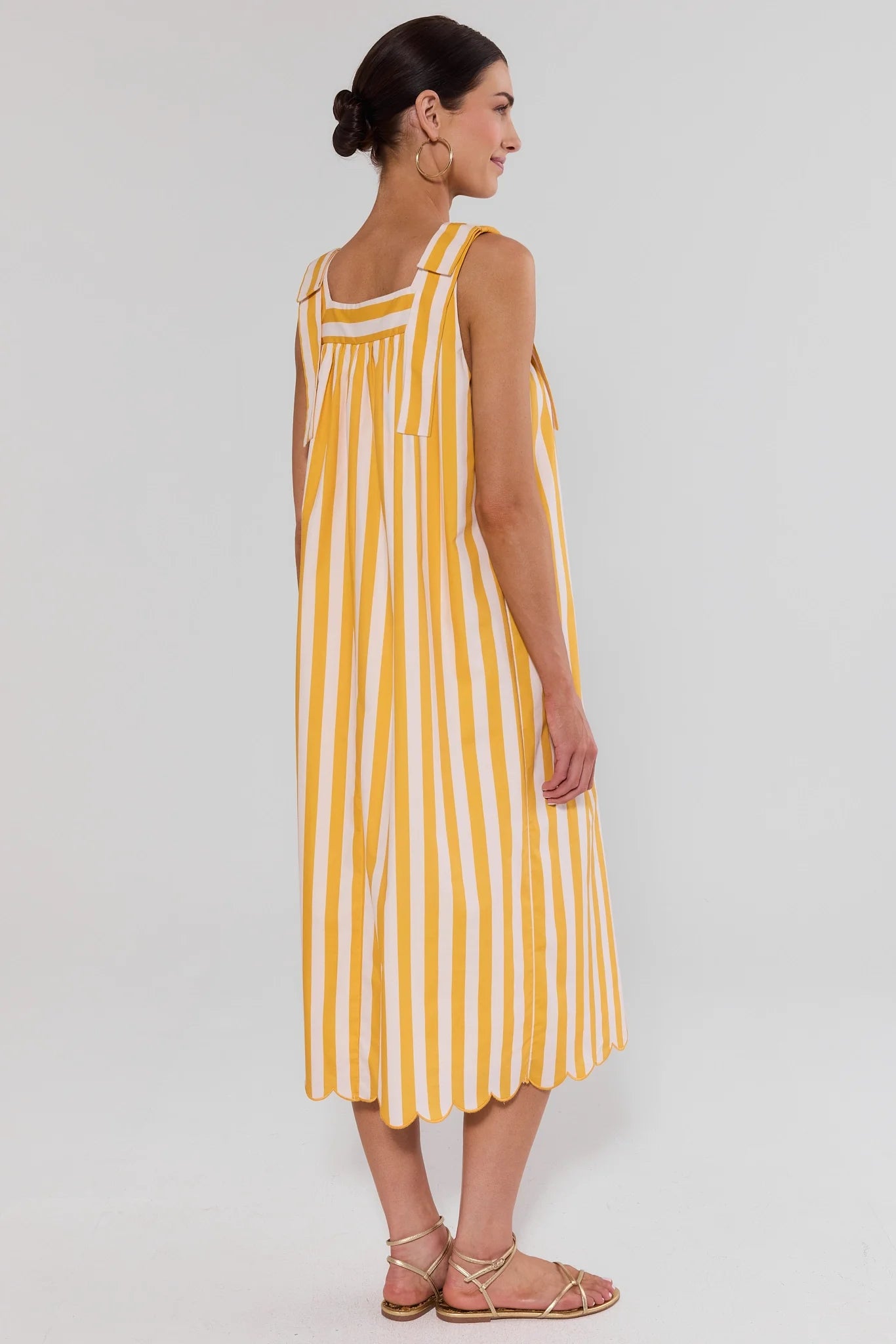 Woman standing wearing a yellow and white striped dress on a plain background