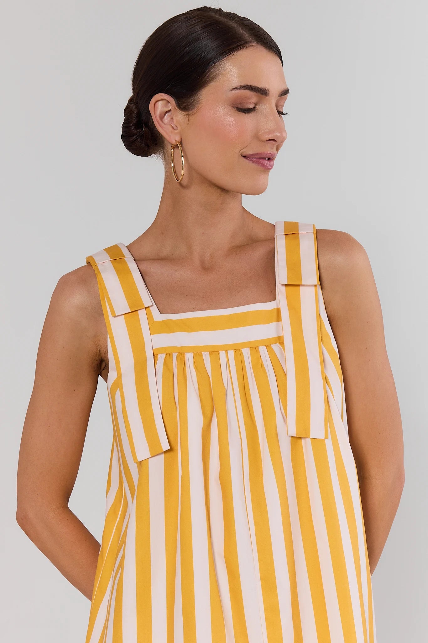 close up Woman wearing a yellow and white striped dress against a plain background