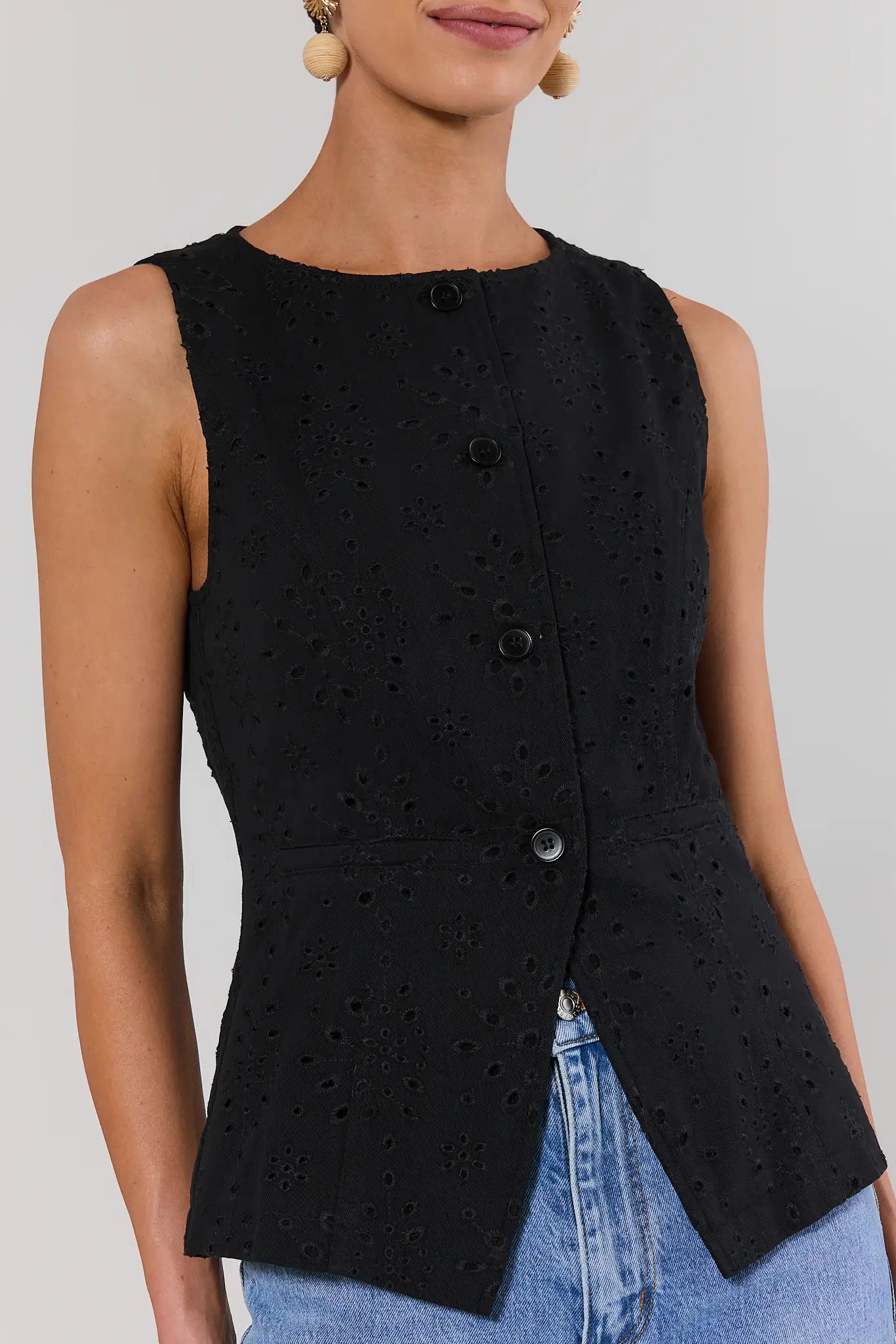 close up Black sleeveless top with button details worn by a person on a plain background