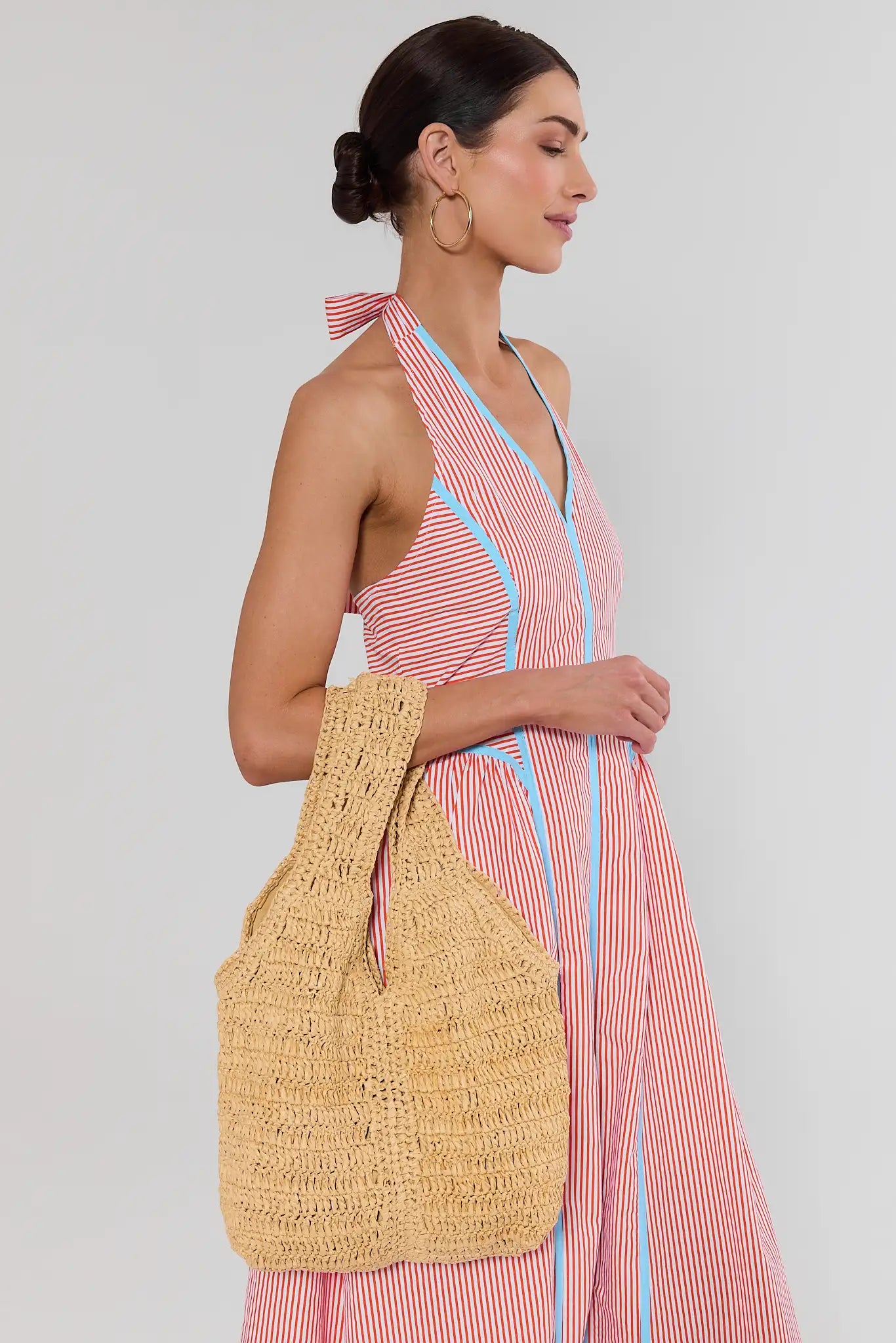 Woman wearing a pink and blue striped dress holding a yellow woven bag against a white background