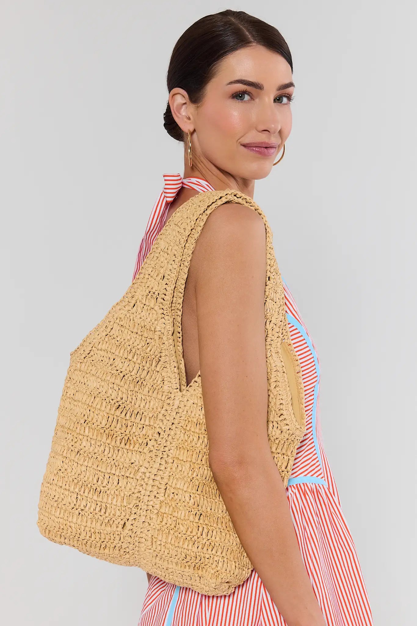 Woman wearing a yellow woven top and striped dress against a plain background