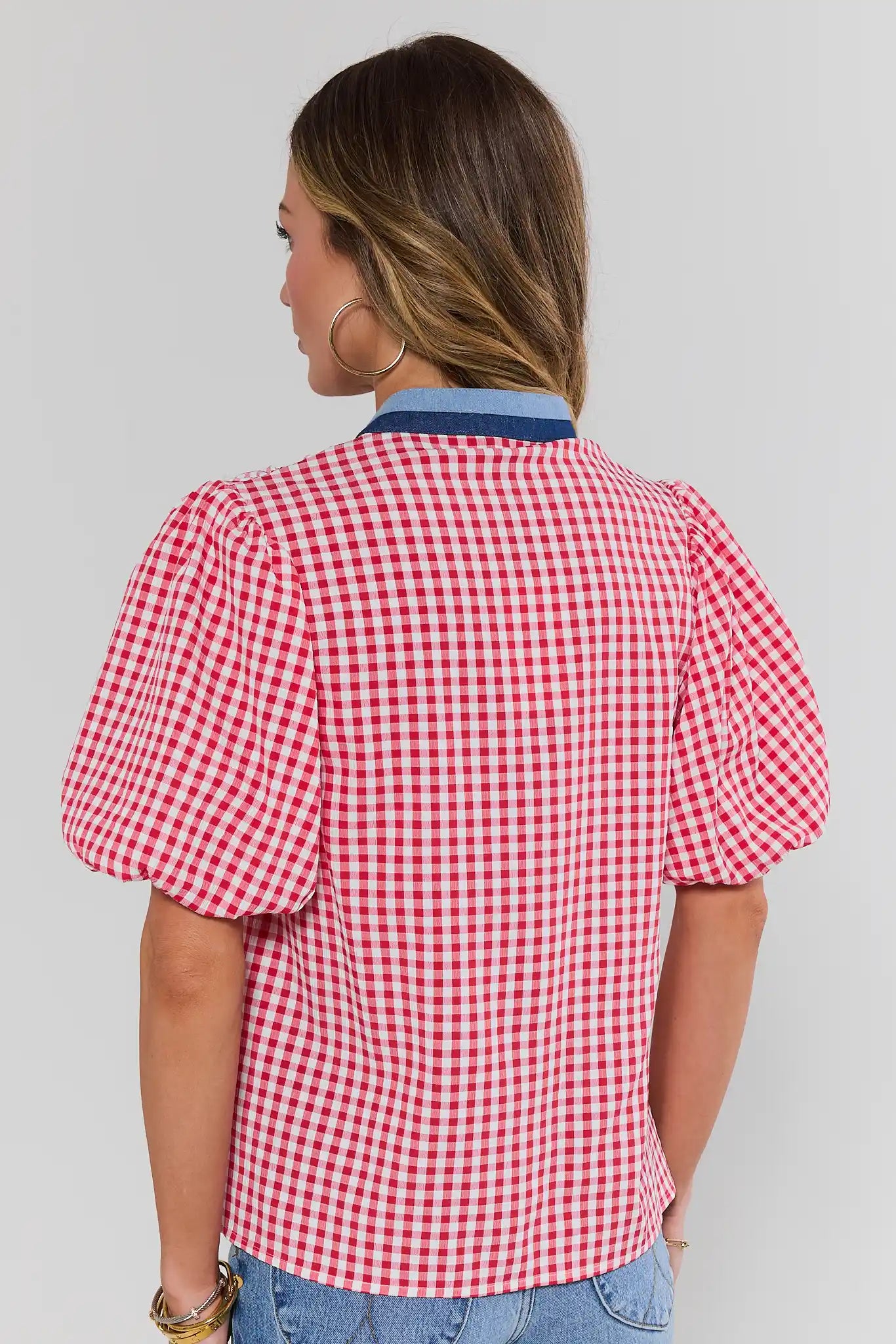 Woman standing wearing a red and white checkered blouse with blue jeans on a plain background