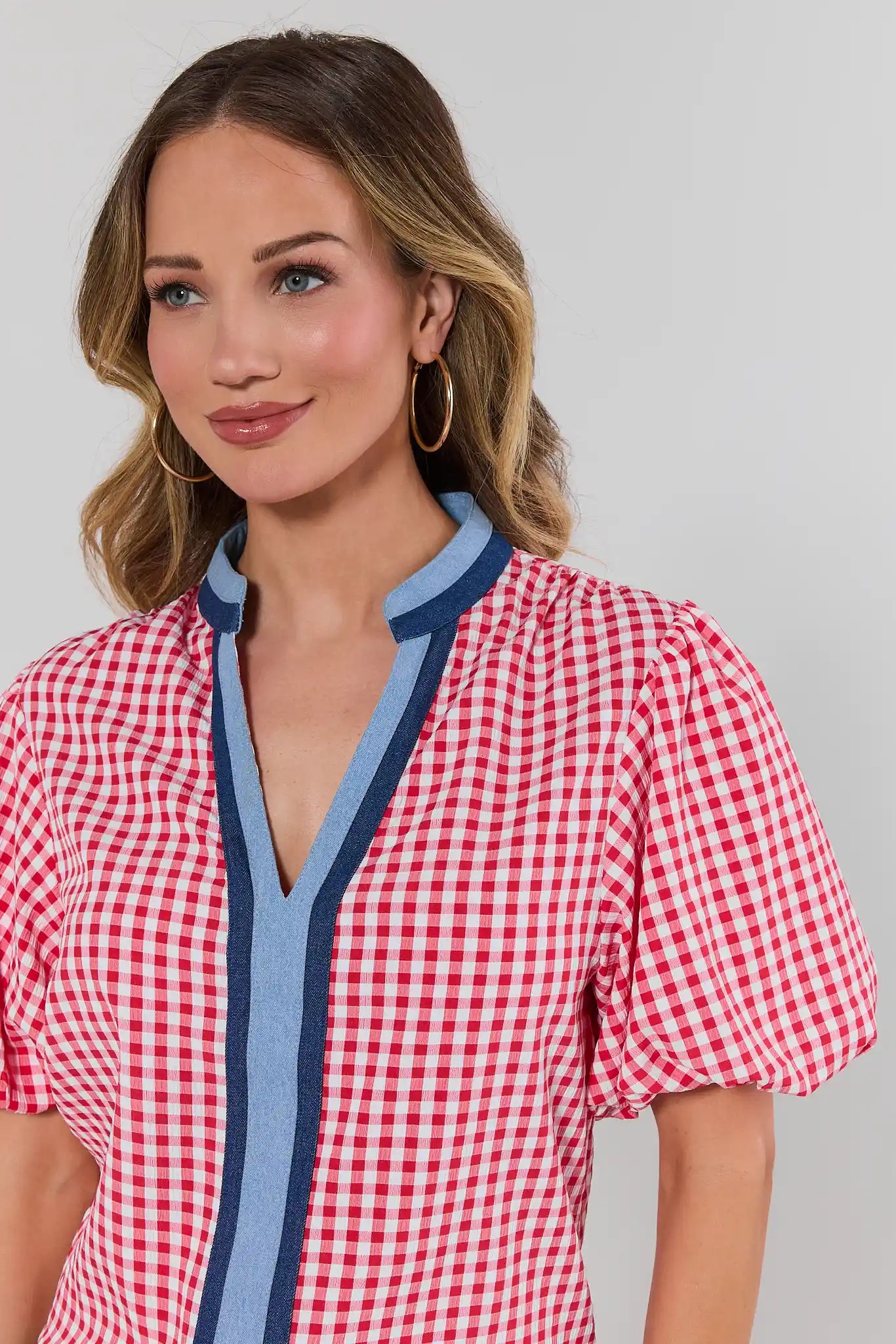 Woman wearing a red and white checkered blouse with blue trim on a plain background close up