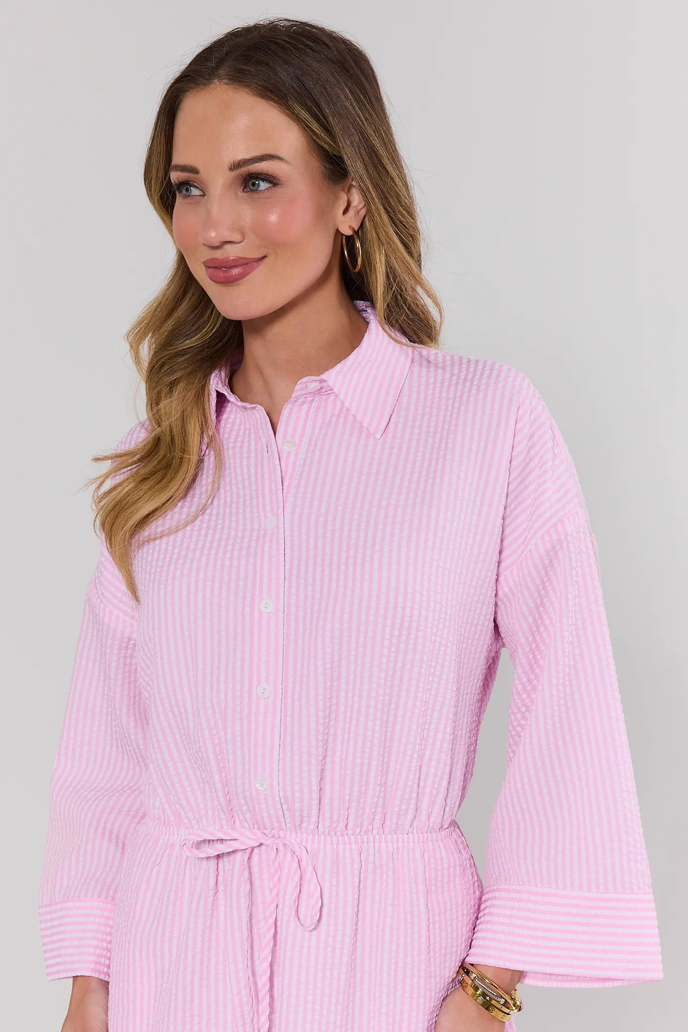 Woman wearing a pink striped shirt dress against a gray background close up