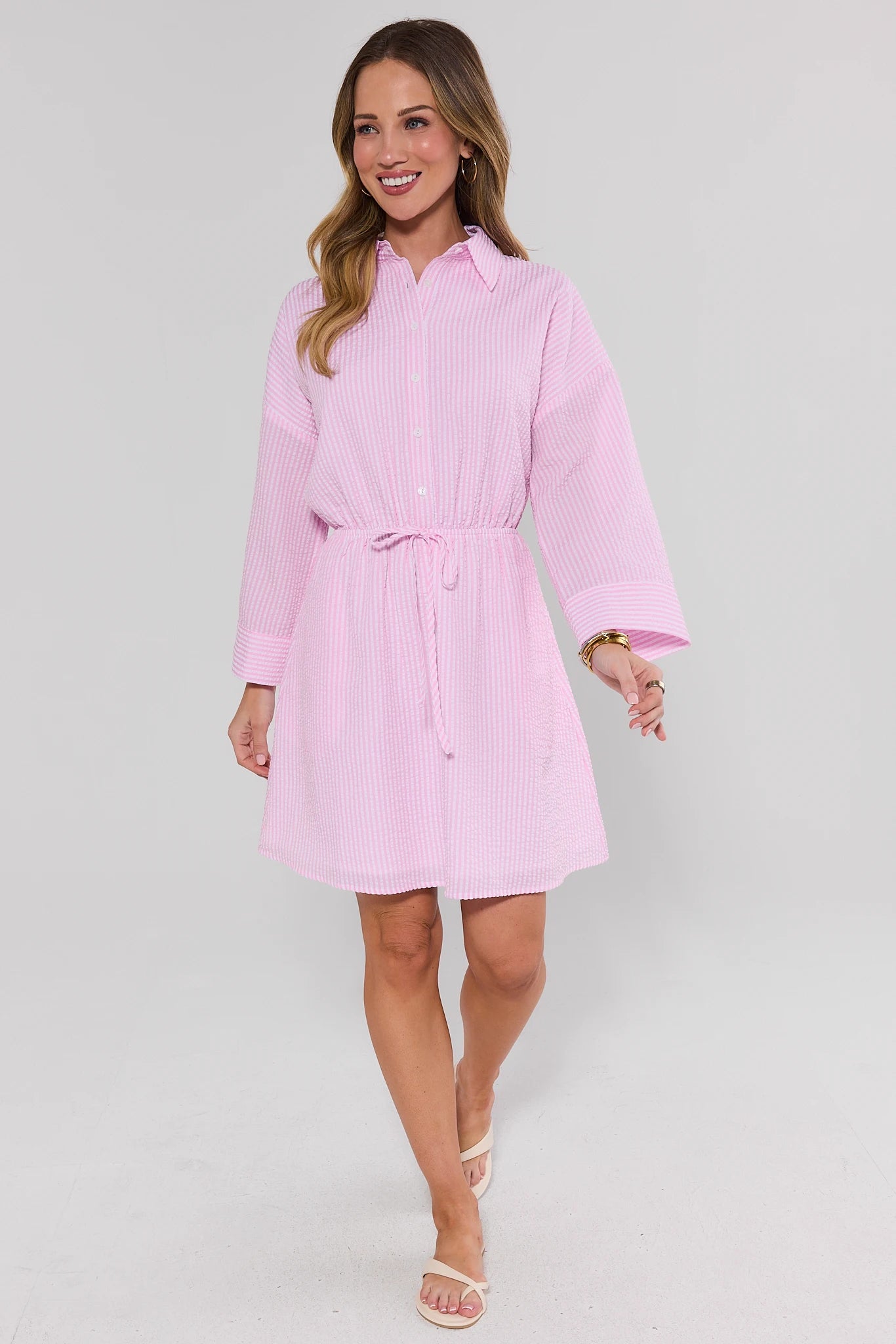 Woman walking wearing a pink dress with a belt on a light gray background