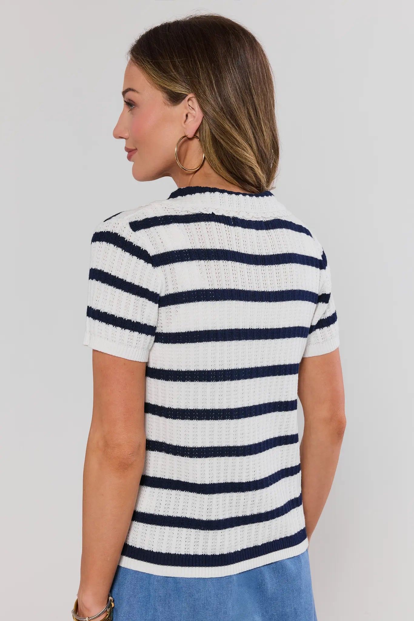 Woman wearing a white and navy striped shirt against a plain background standing