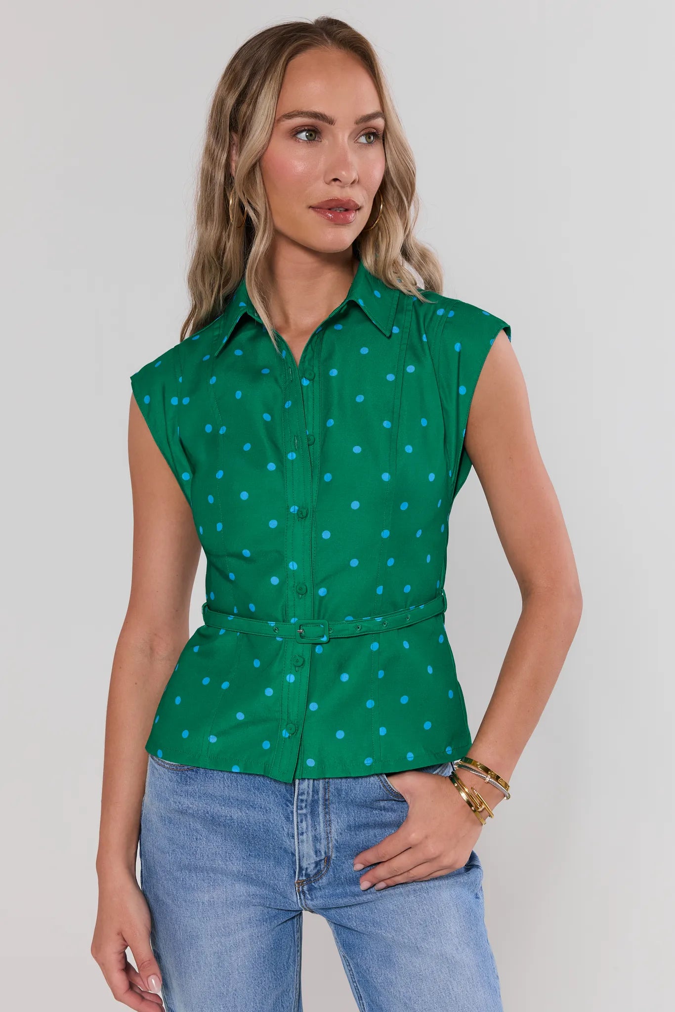 Woman wearing a green sleeveless polka dot shirt and blue jeans against a white background