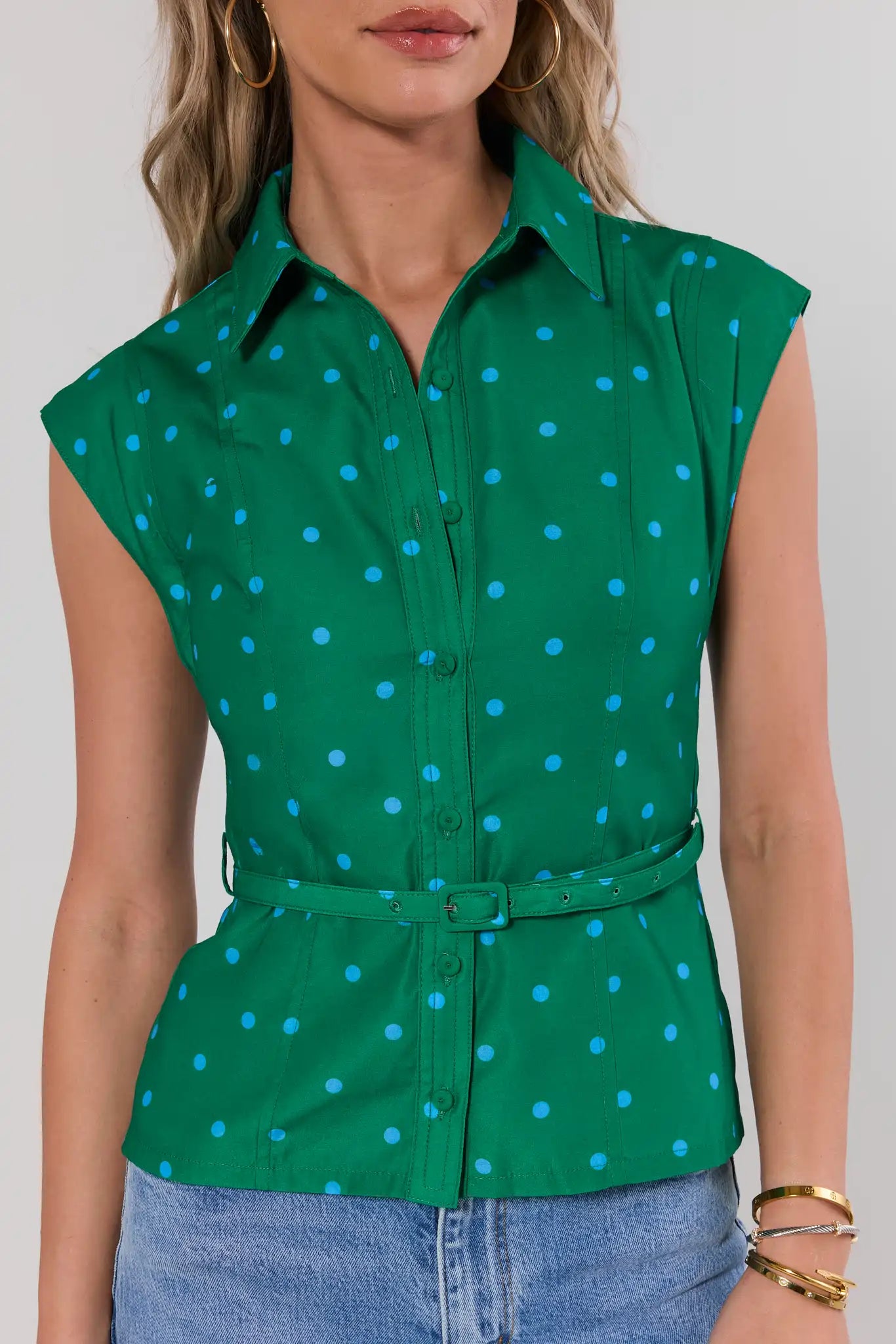 Green sleeveless shirt with white polka dots worn by a person on a plain background close