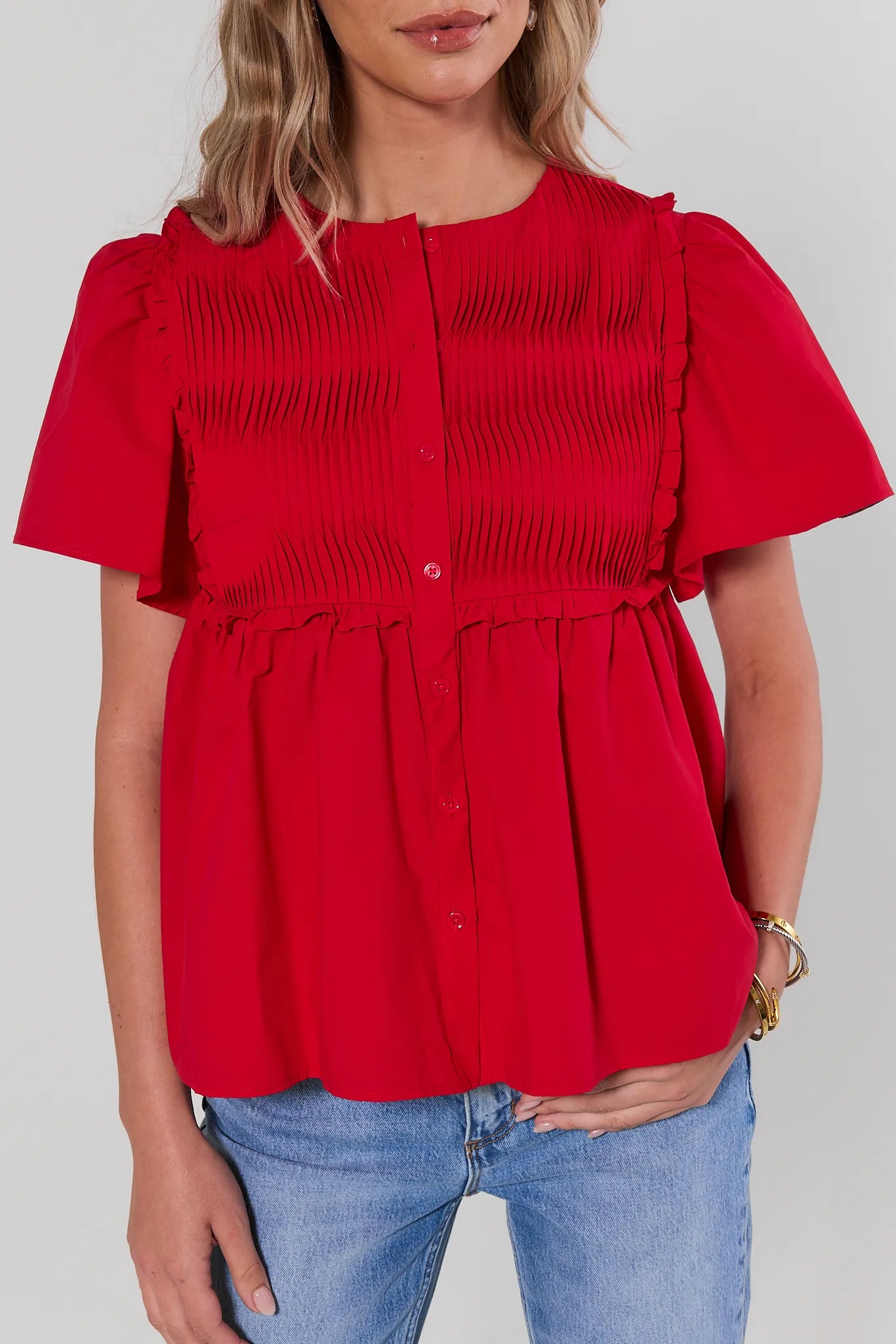 Red blouse with ruffled details worn by a person on a plain background close up