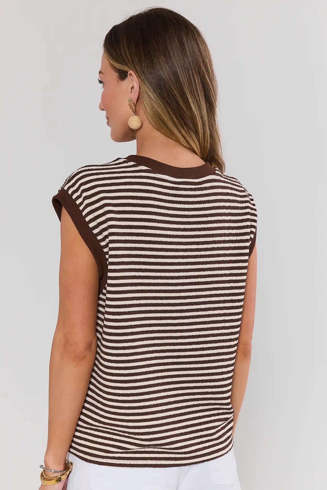 Woman standing wearing a brown and white striped sleeveless top against a plain background