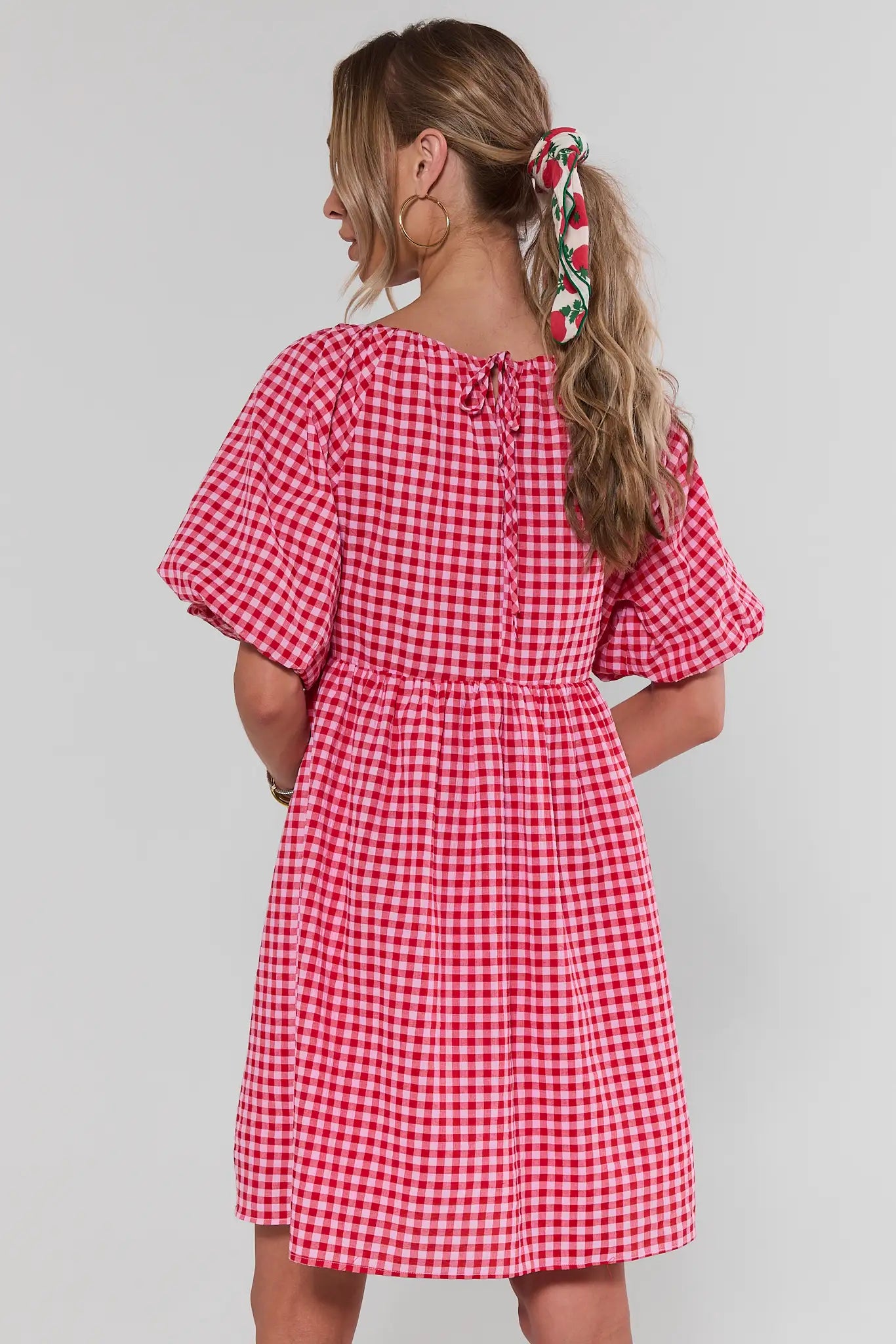 Woman standing wearing a red and white checkered dress against a plain background