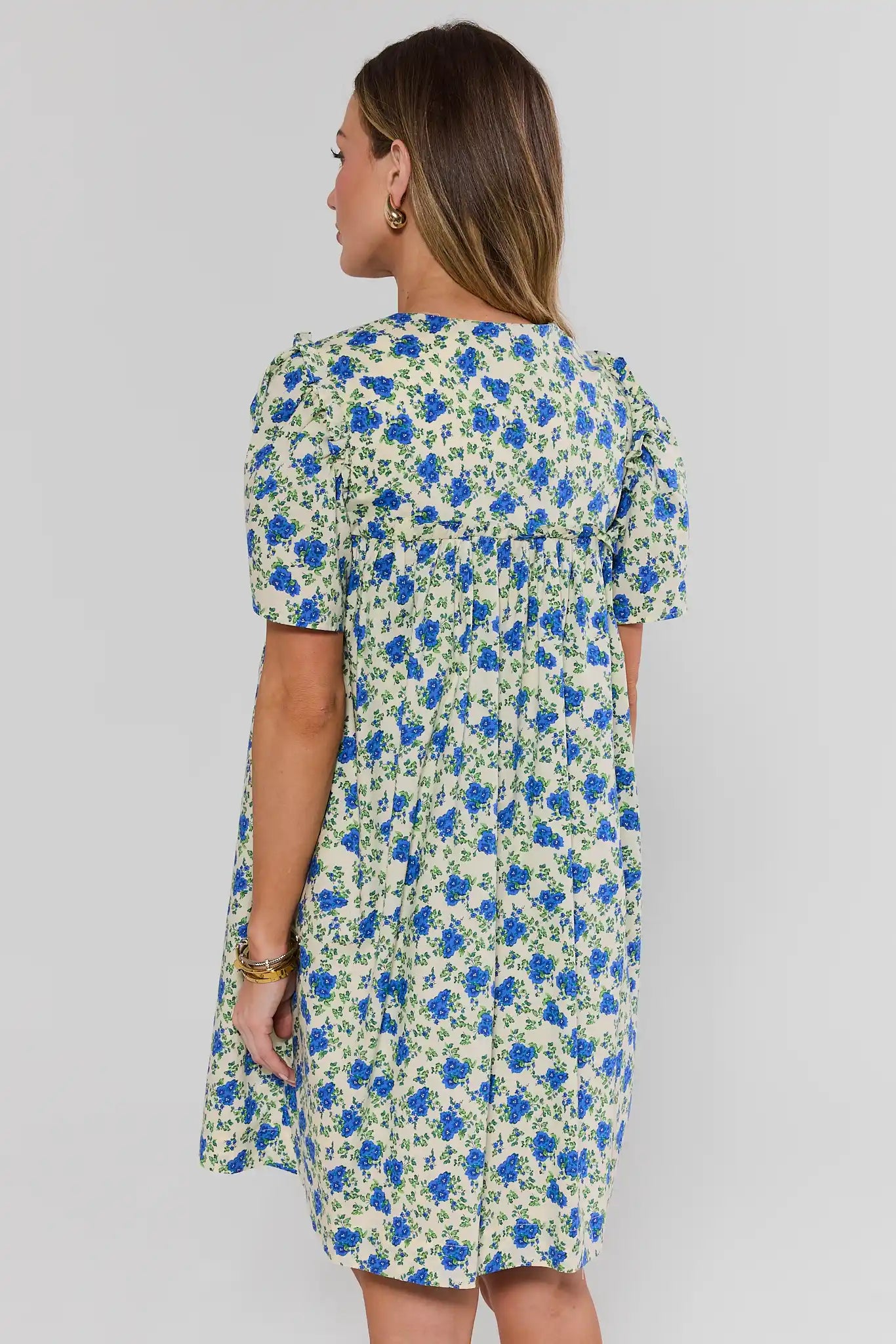 Woman wearing a floral dress with blue and green flowers on a plain background standing