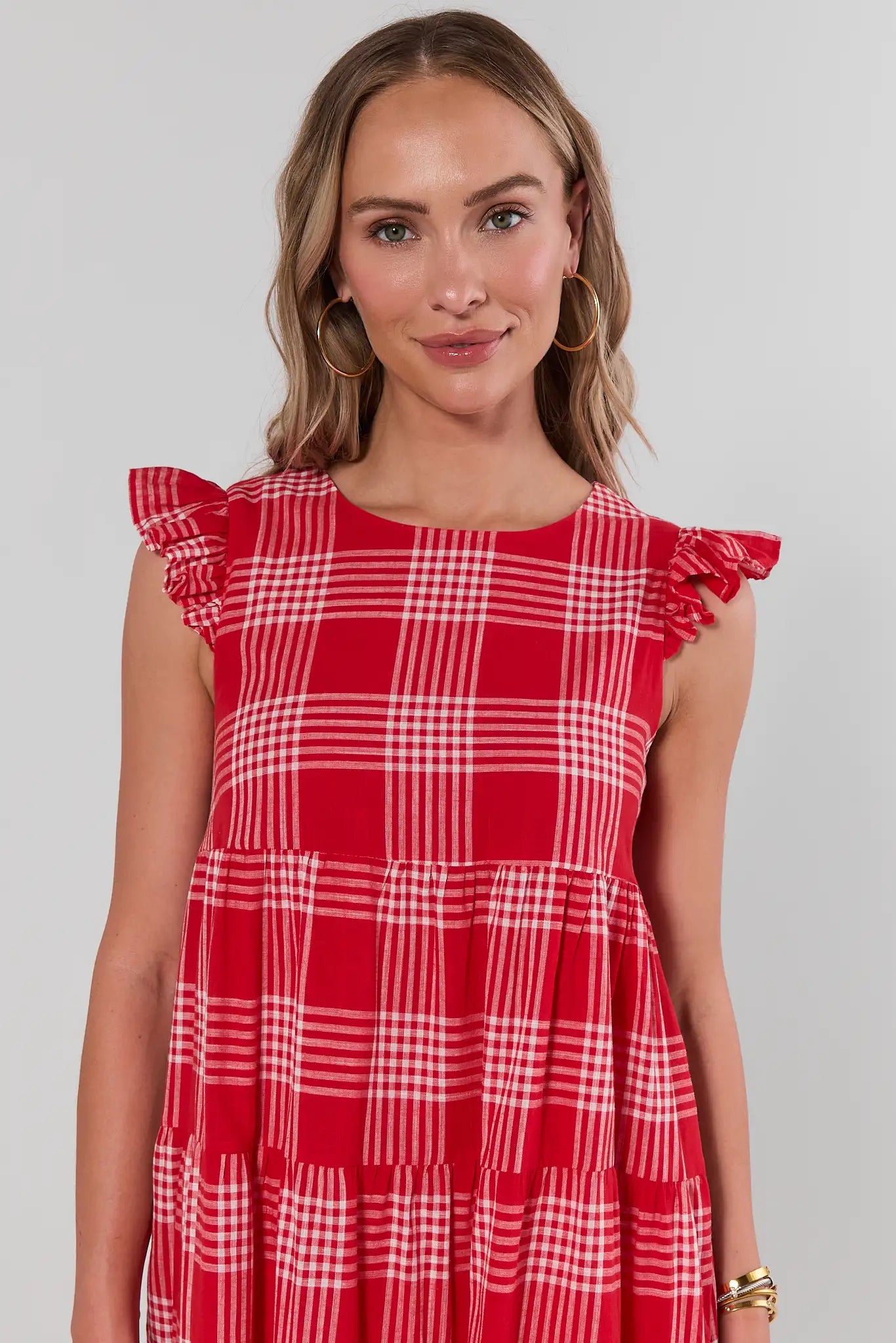 Woman wearing a red and white checkered dress with ruffled sleeves on a plain background close up