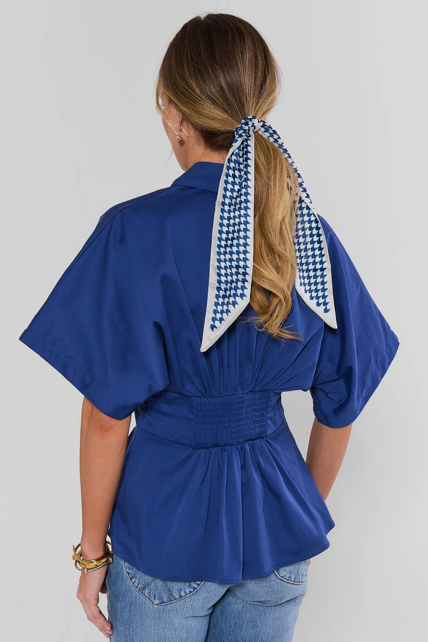 Person wearing a blue top with a houndstooth patterned hair tie on a plain background