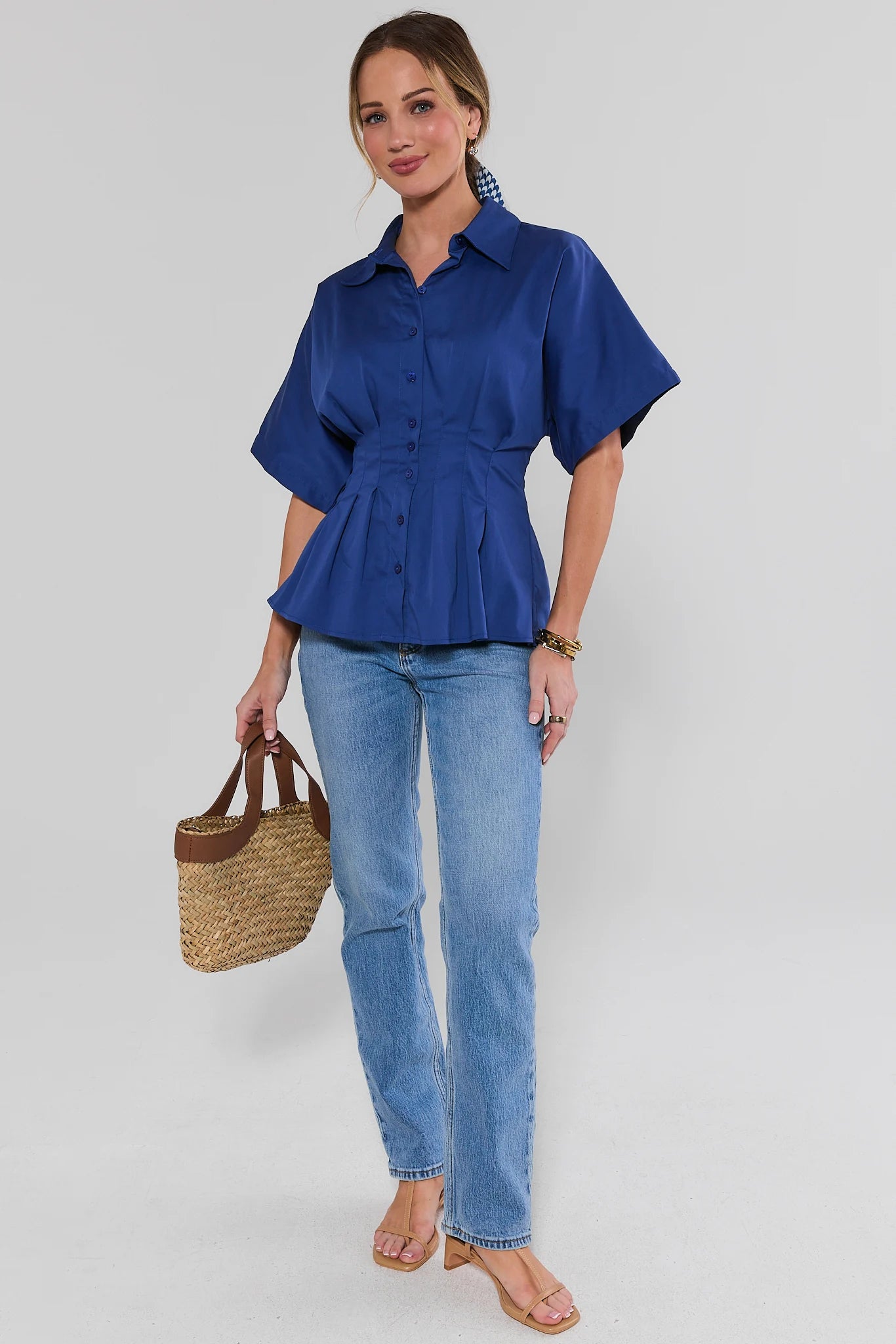 Woman wearing a blue shirt and jeans holding a straw bag on a white background