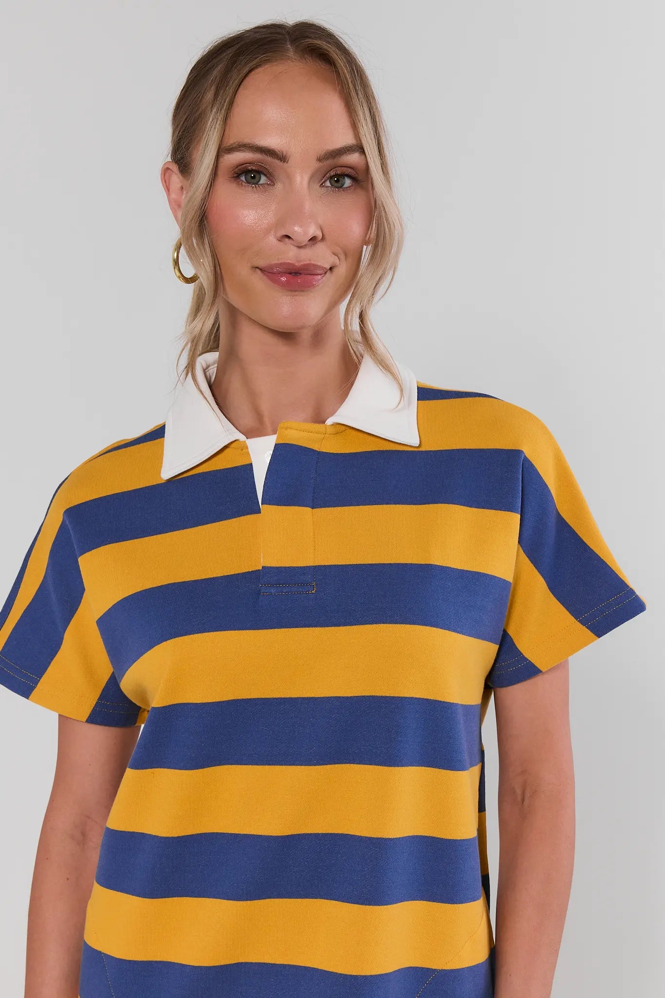 close up Woman wearing a blue and yellow striped polo shirt against a plain background