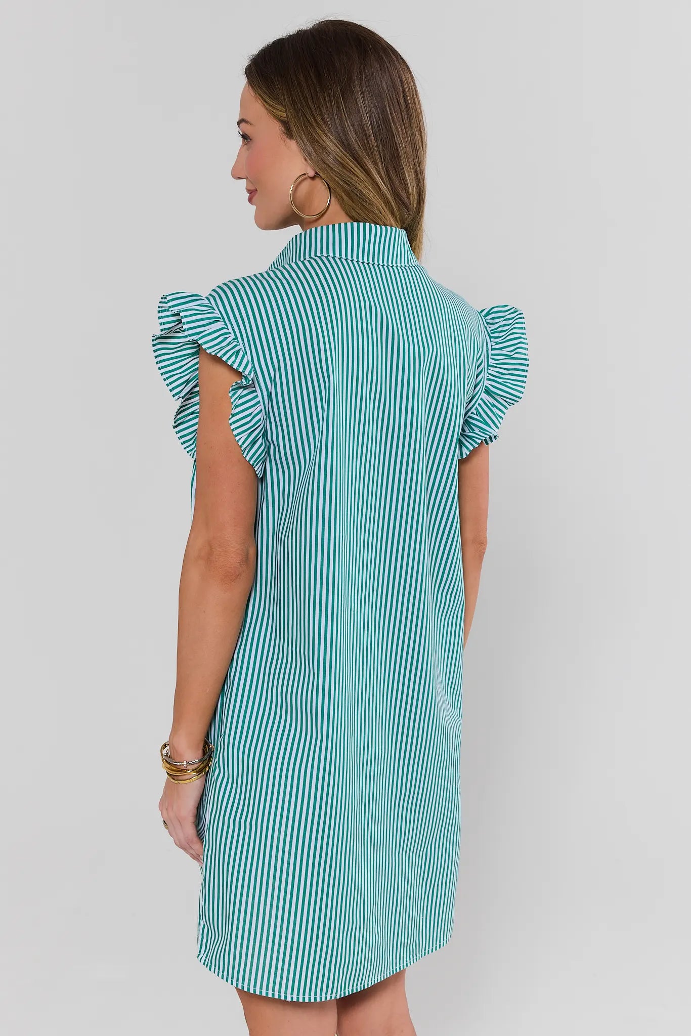 Woman wearing a teal and white striped dress with ruffled sleeves on a plain background standing