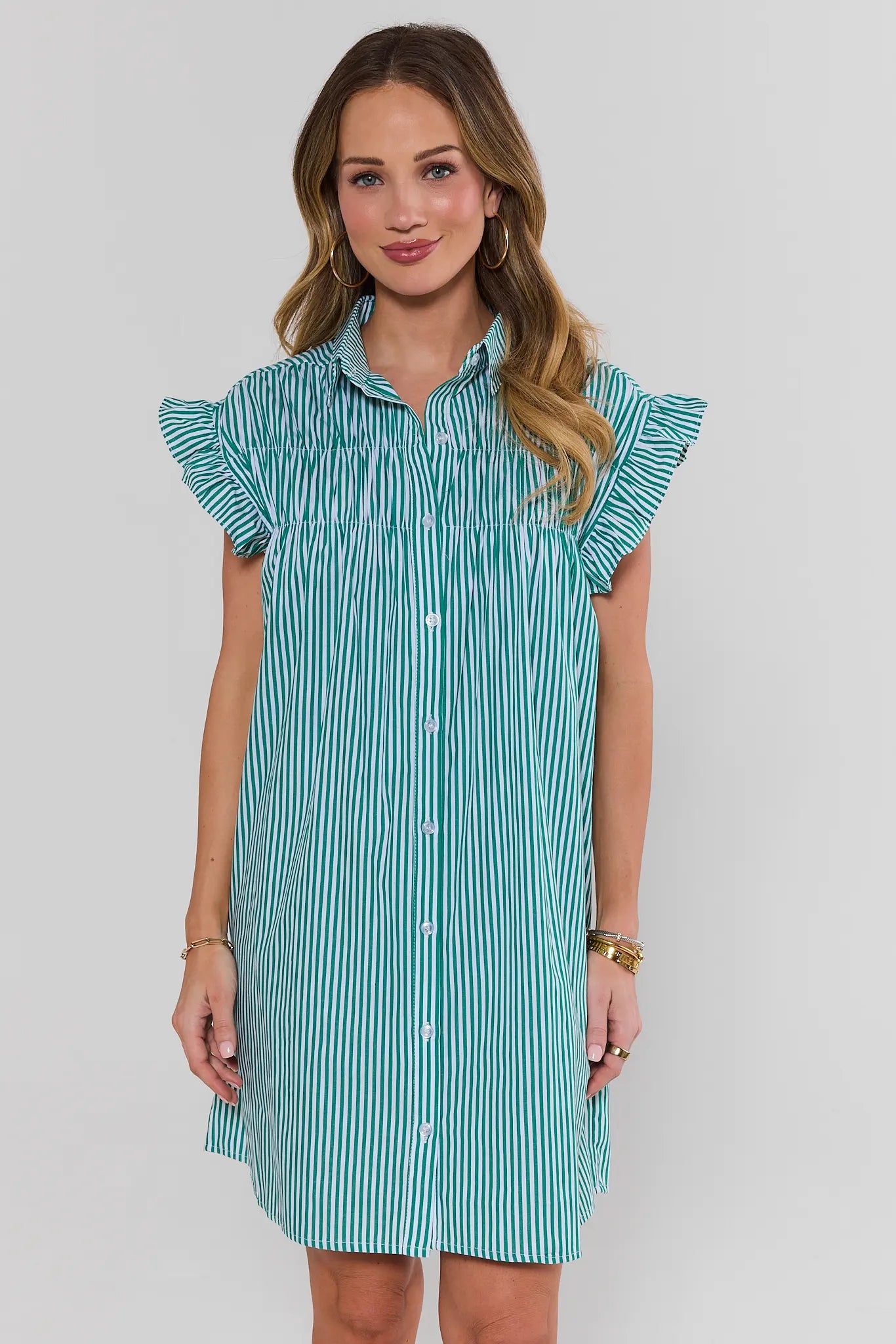 Woman wearing a teal and white striped dress with ruffled sleeves on a gray background