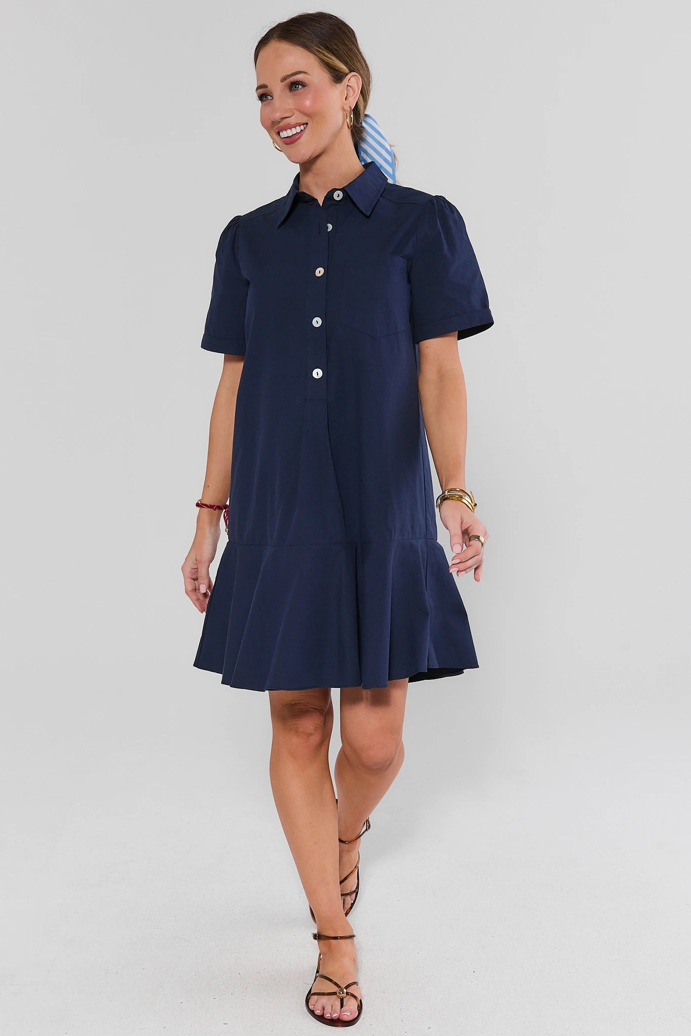 Woman wearing a navy blue dress with white buttons on a light gray background