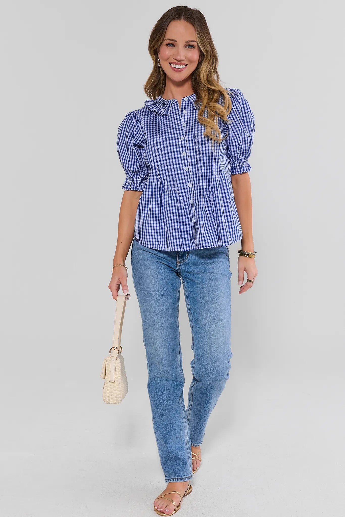 Woman standing wearing a blue checkered blouse and jeans on a plain background