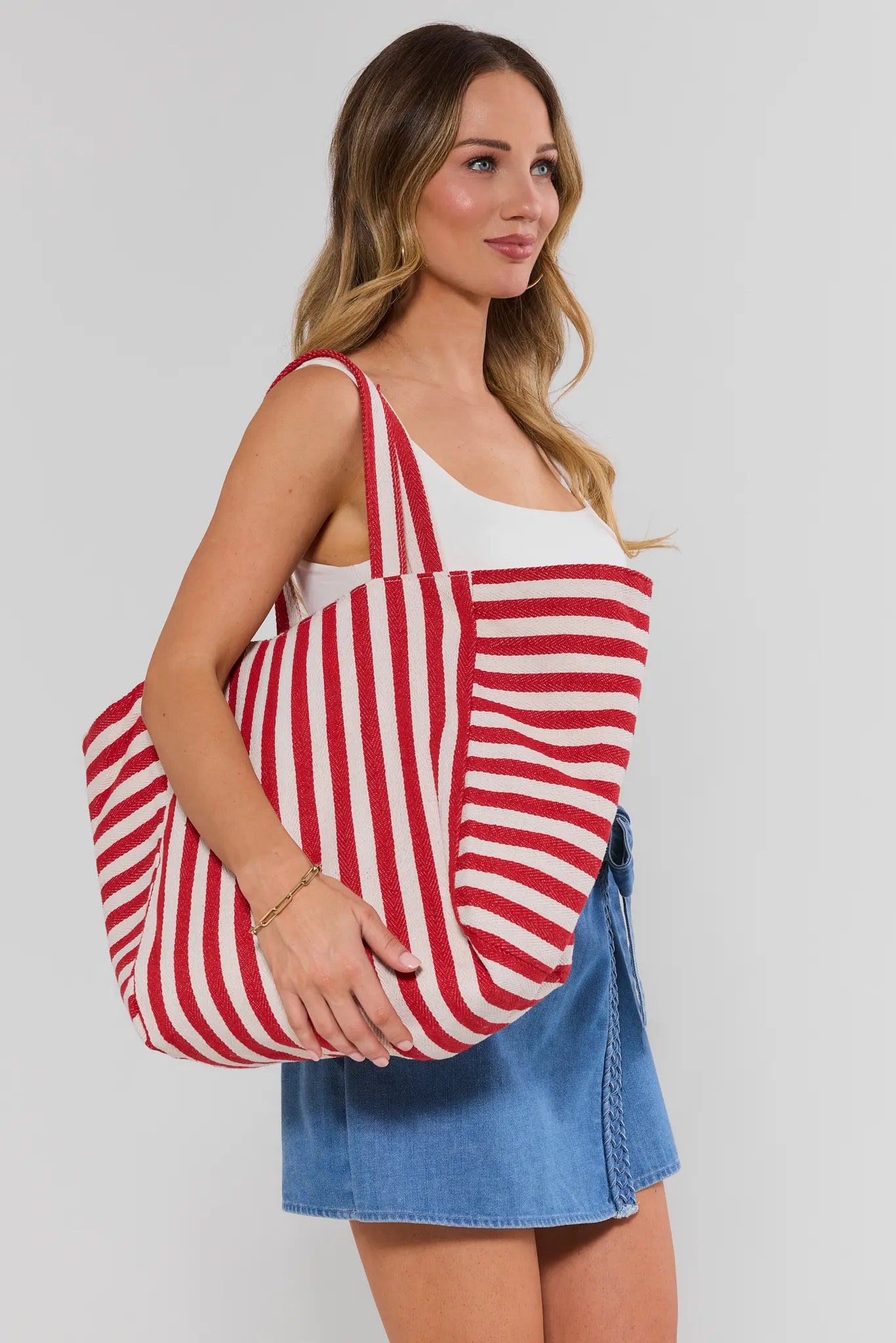 Woman holding a red and white striped bag against a plain background