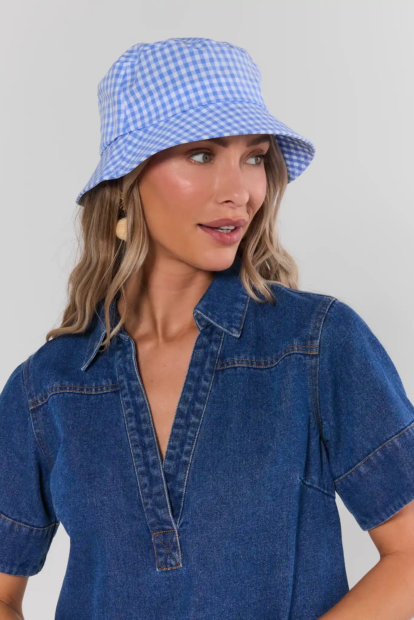 Woman wearing a blue checkered bucket hat and denim shirt against a gray background
