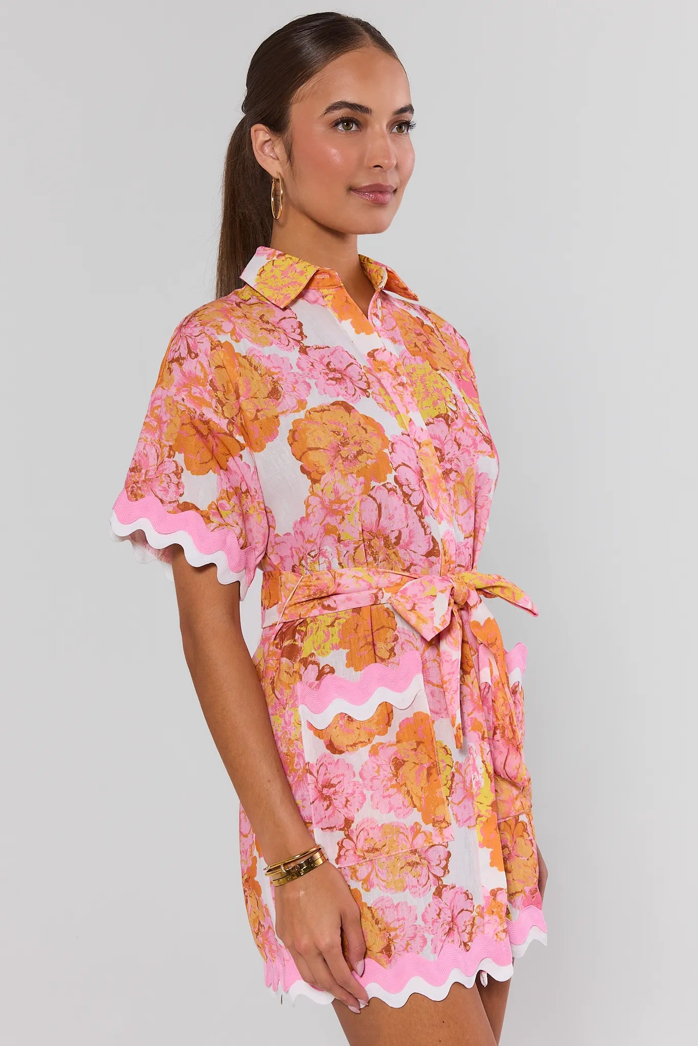 Woman wearing a floral dress with pink and orange flowers on a plain background side