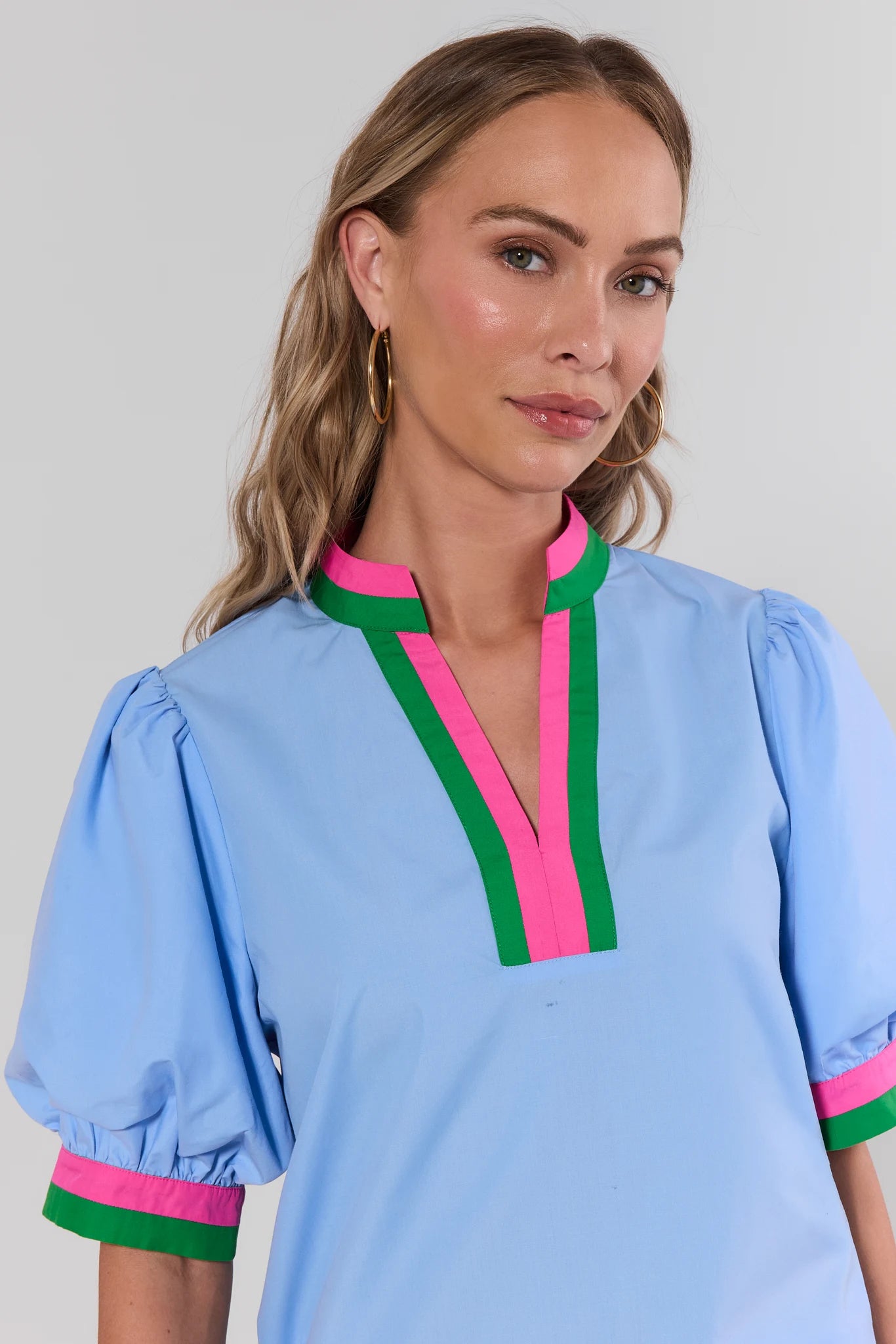 Woman wearing a light blue blouse with pink and green accents on a plain background close up