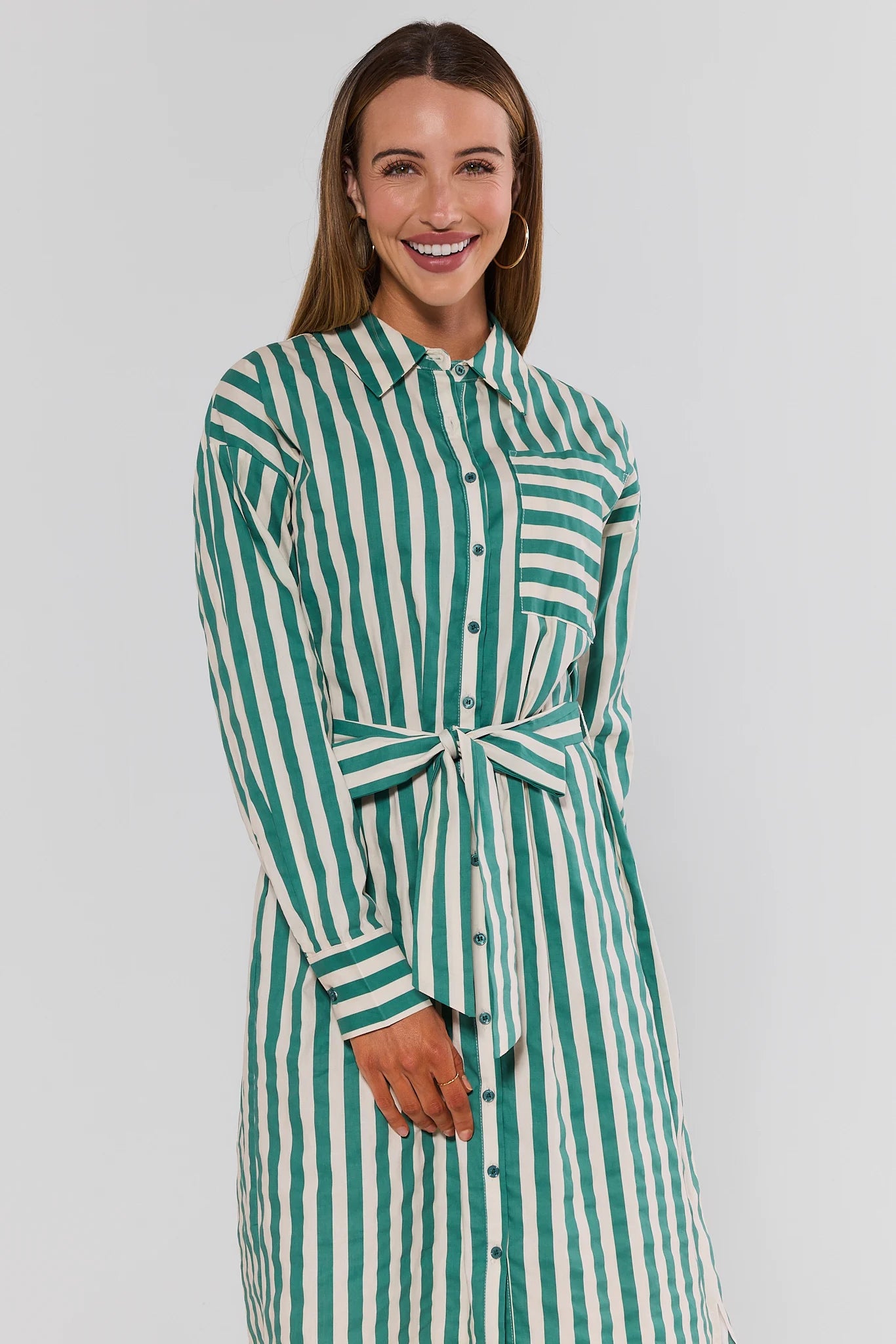 Woman wearing a green and white striped dress against a plain background standing