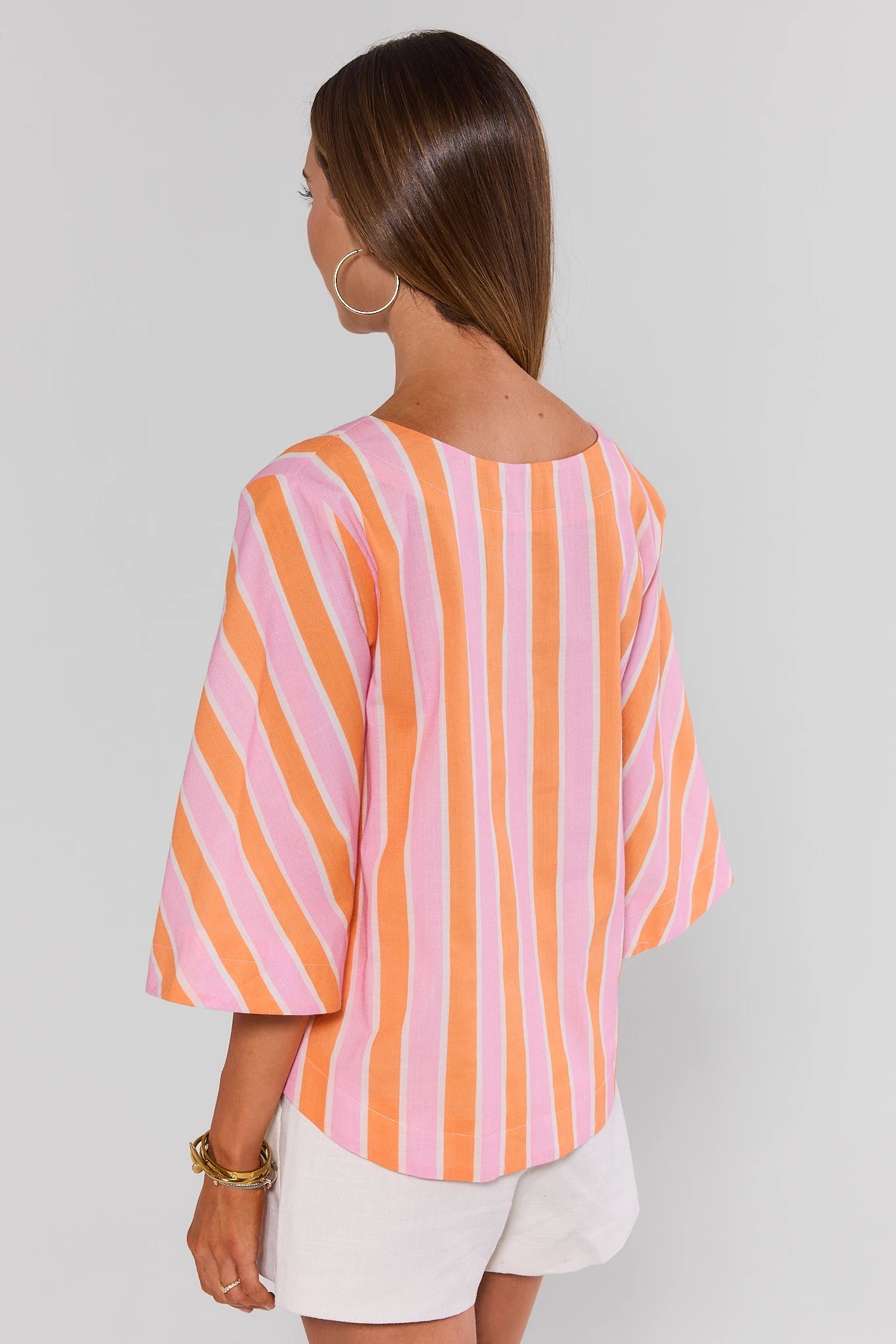 Woman standing wearing a colorful striped shirt with a plain background