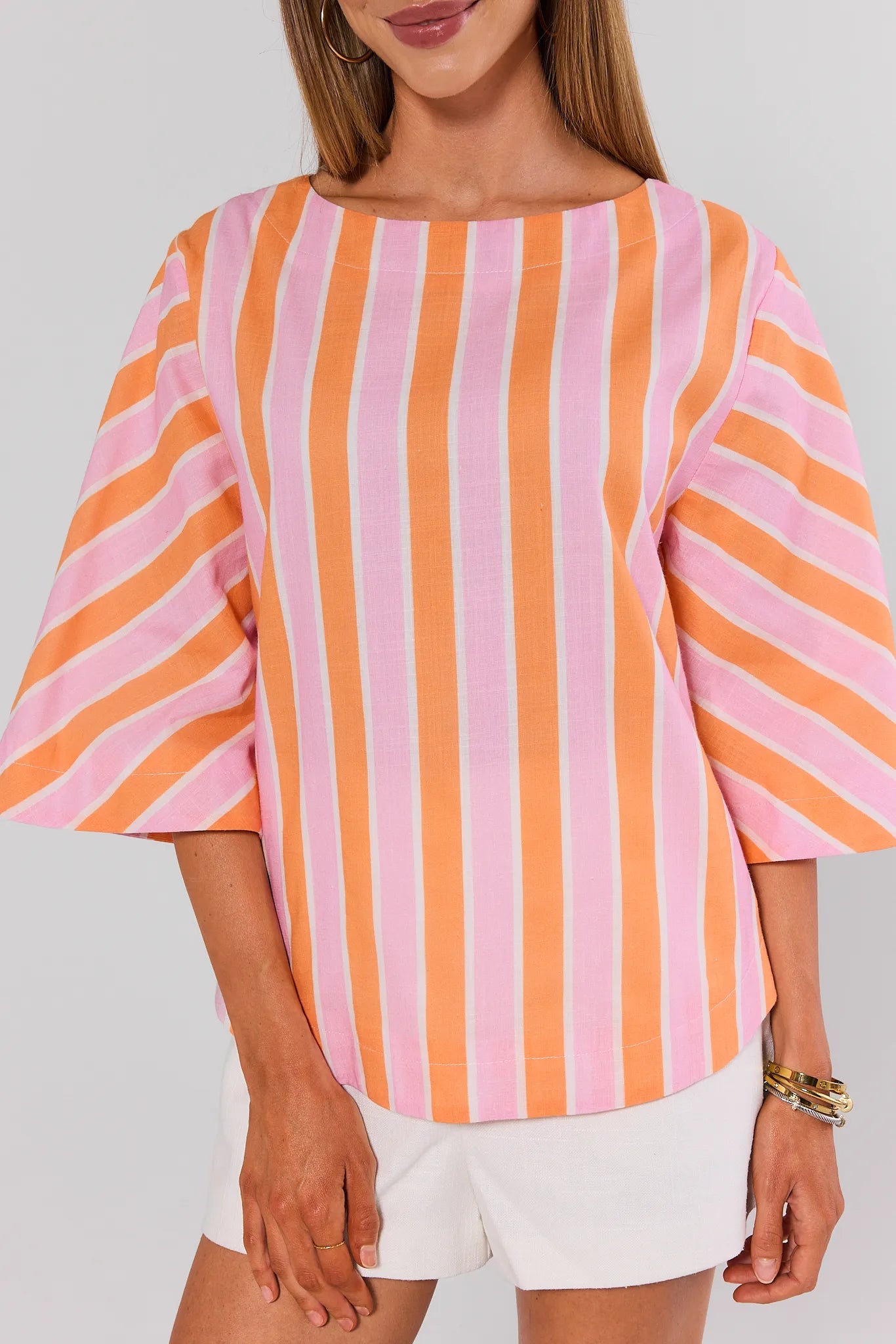 Woman wearing a pink and orange striped shirt with white shorts on a plain background close up